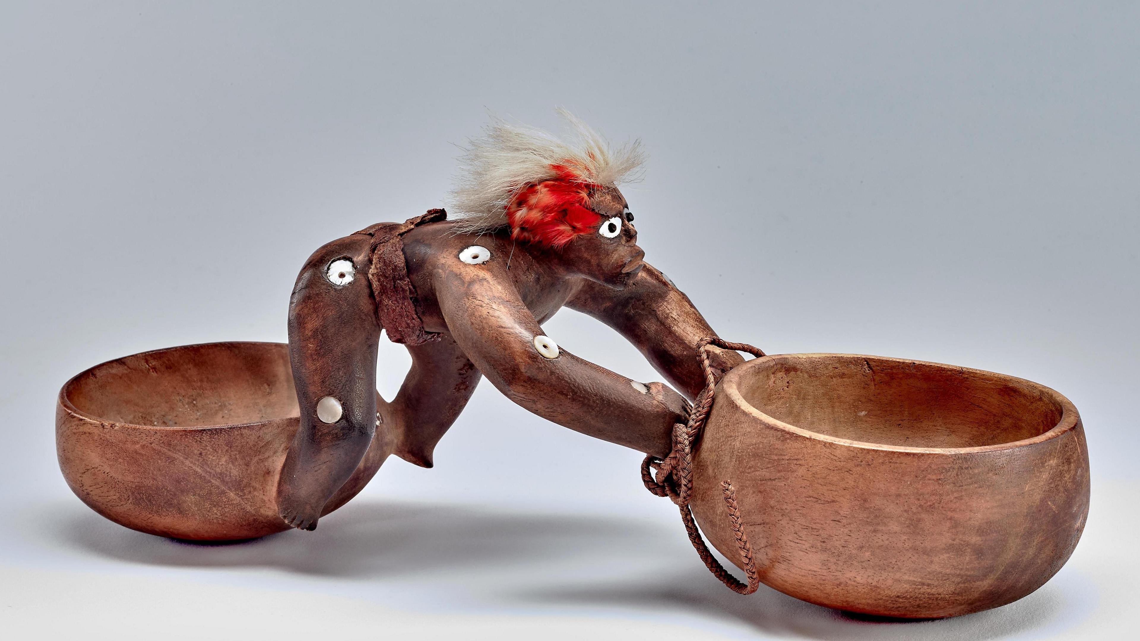 Two carved wooden bowls linked by a carved wooden human figure.