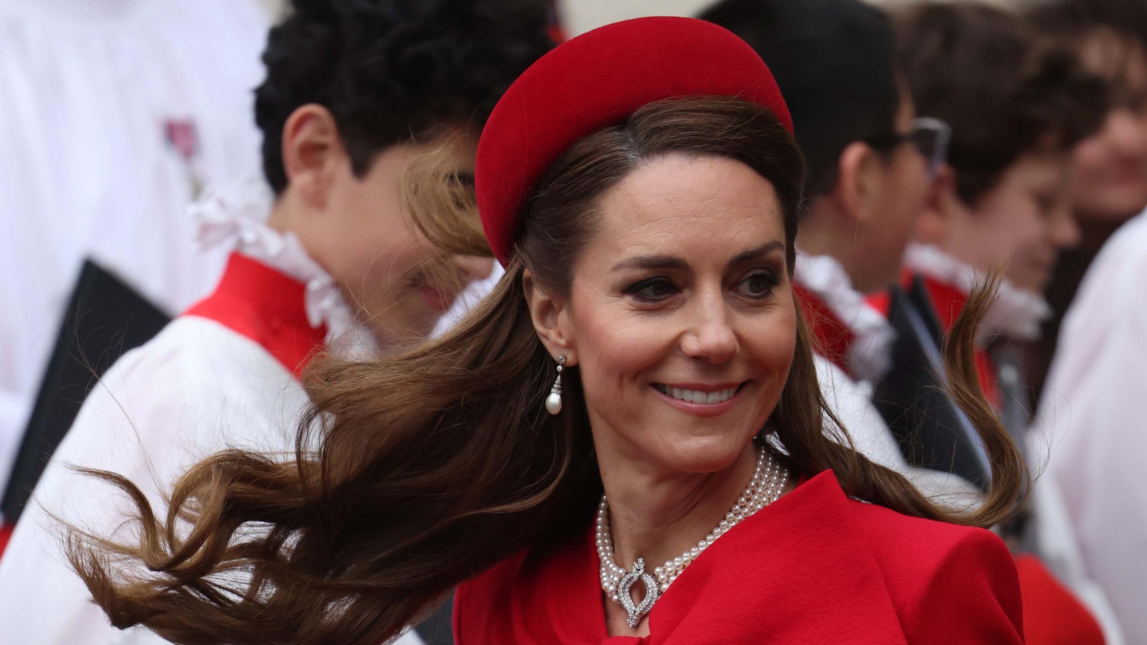 Catherine, Princess of Wales, is smiling while wearing a matching red hat and dress.