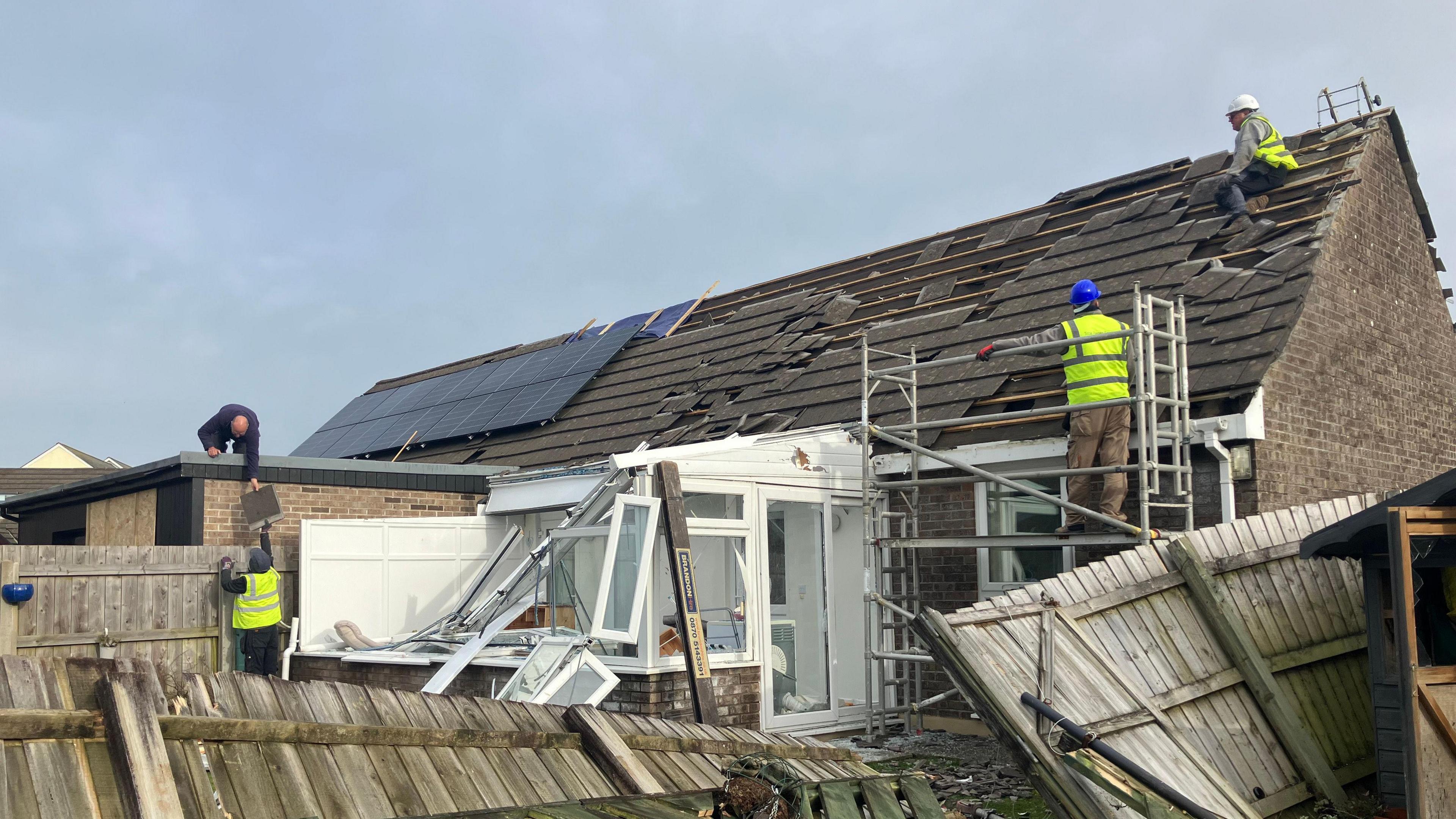 Roofers using scaffolding to access the roof of a badly damaged house and conservatory