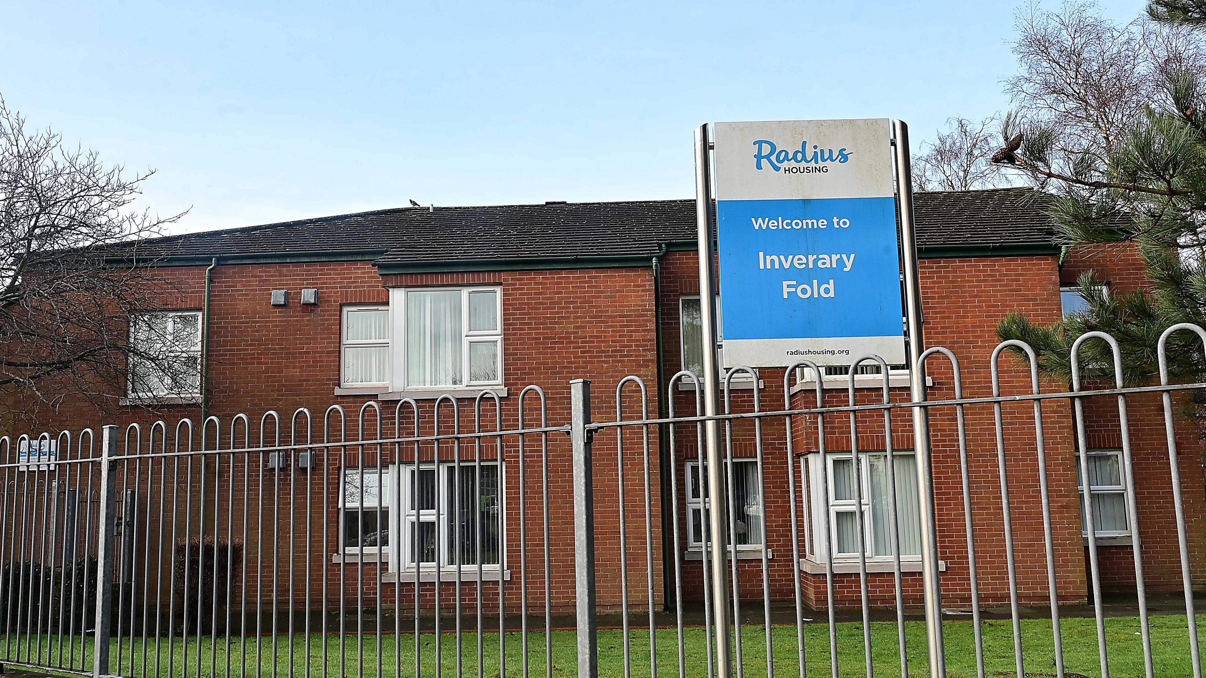 The outside railings of the fold. The building is red brick and a blue and white sign is at the front which says Inverary Fold in white letters.