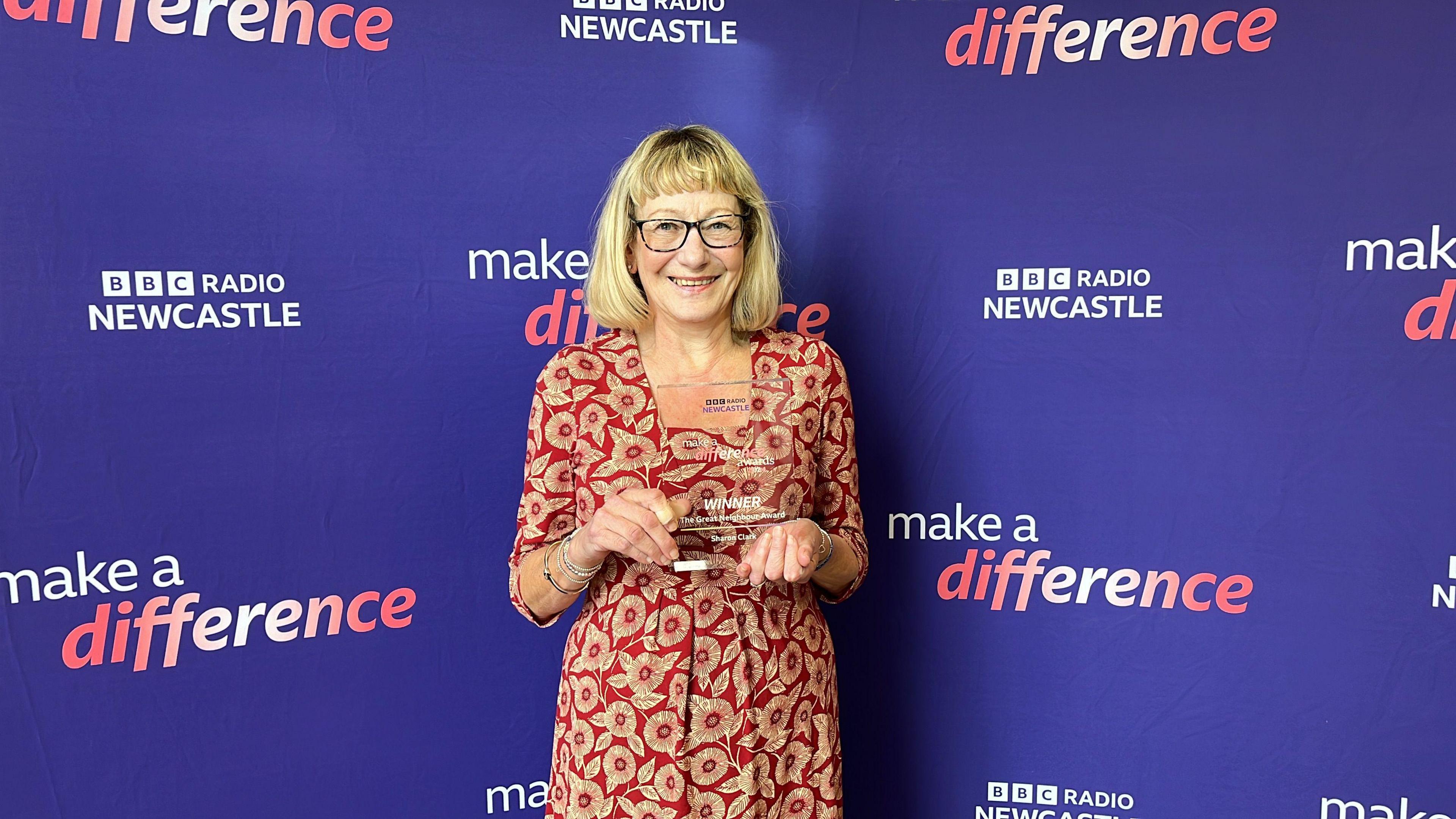 Sharon Clark wearing a floral dress and holding her award.