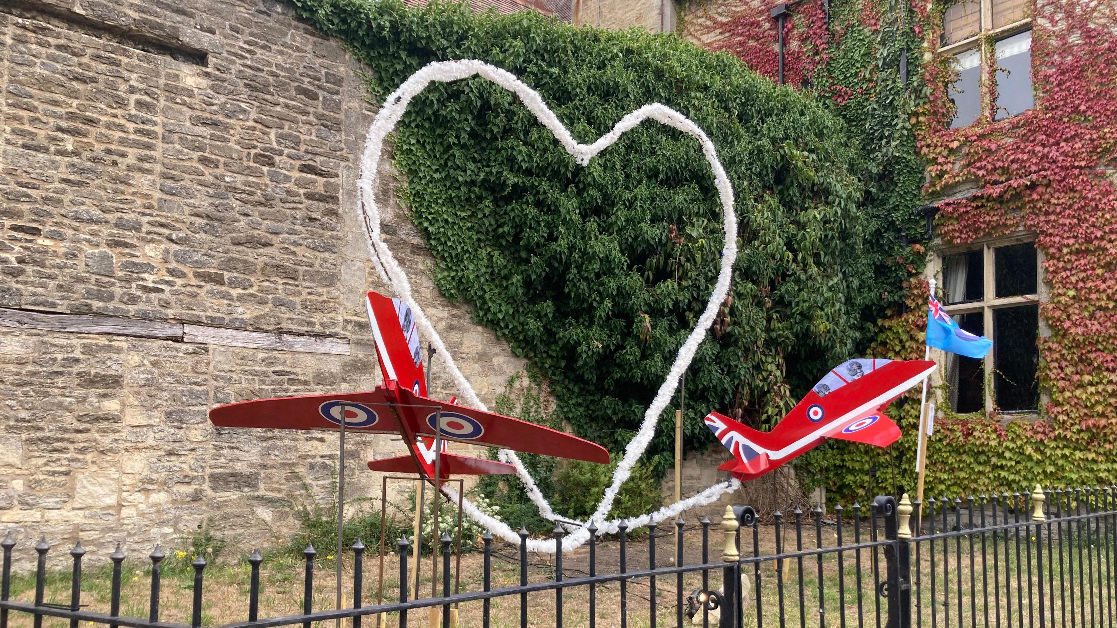 A display of two Red Arrows planes as part of a scarecrow trail. They are both red with union jacks at the back. There is a large heart shape between them. 