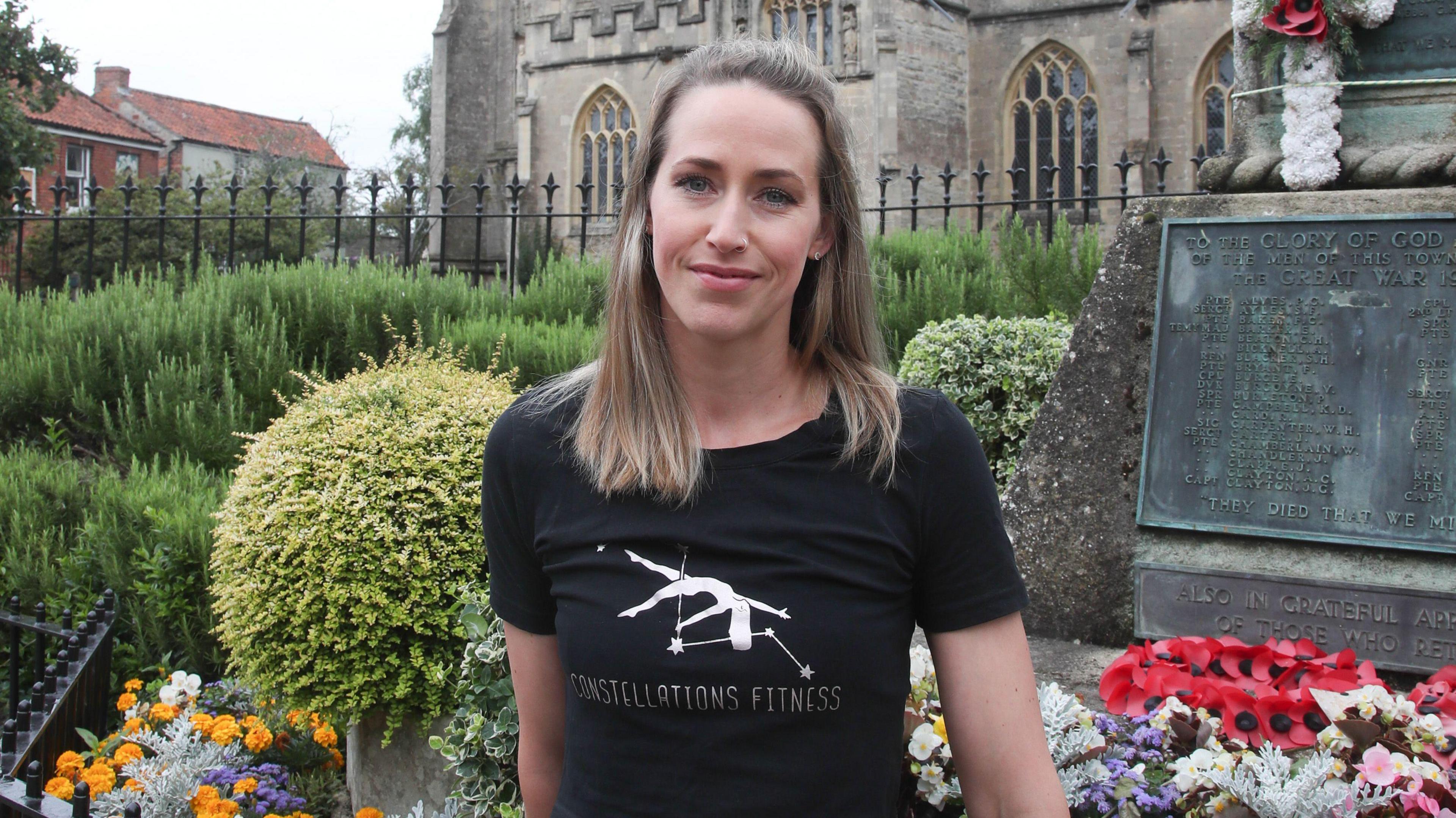 Sophie Badger standing in front of a church. She is wearing a black t-shirt. She has dark blonde hair.