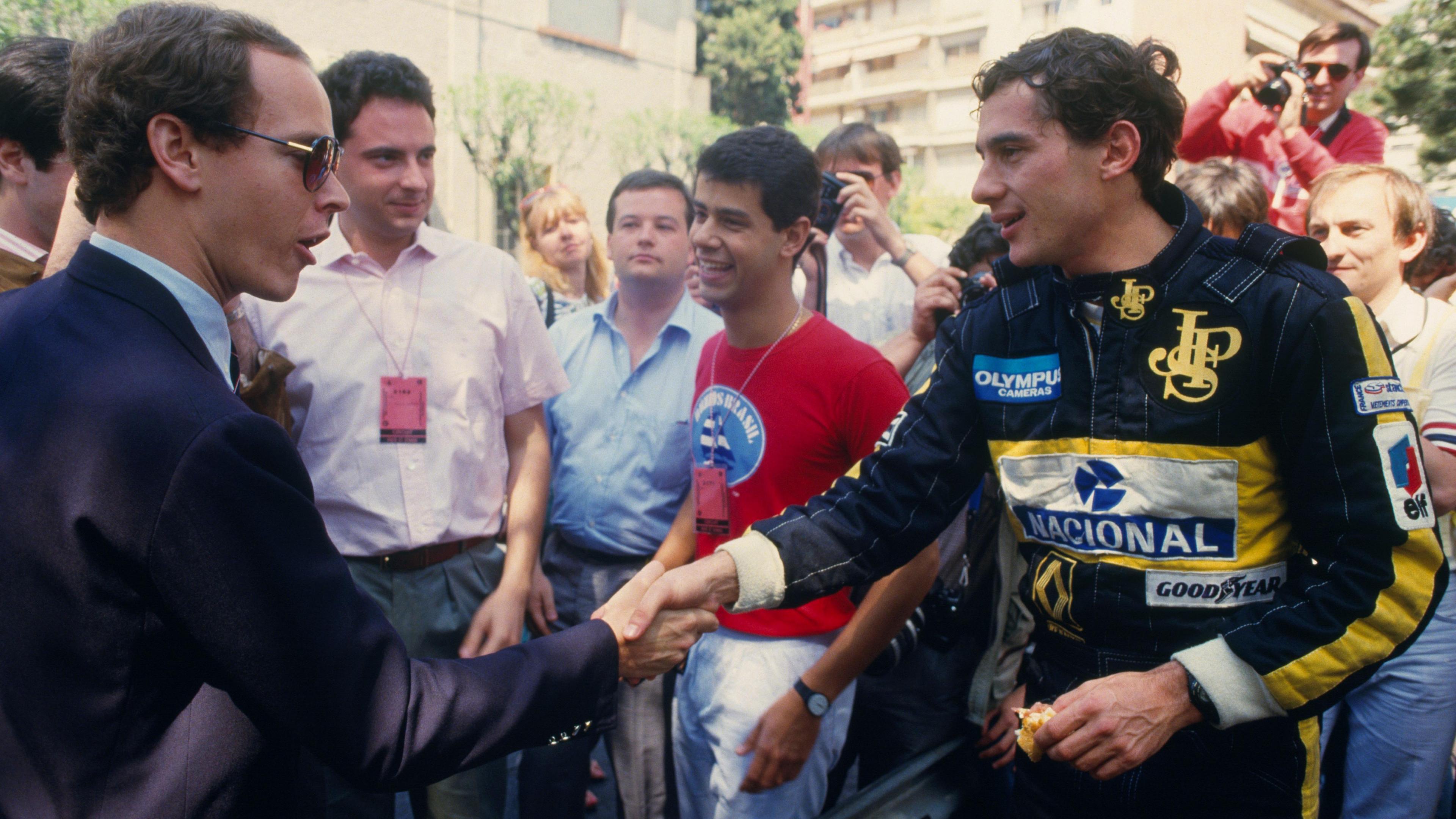 Prince Albert of Monaco shakes hands with Ayrton Senna, wearing a black and gold Lotus overall, at the 1986 Monaco Grand Prix