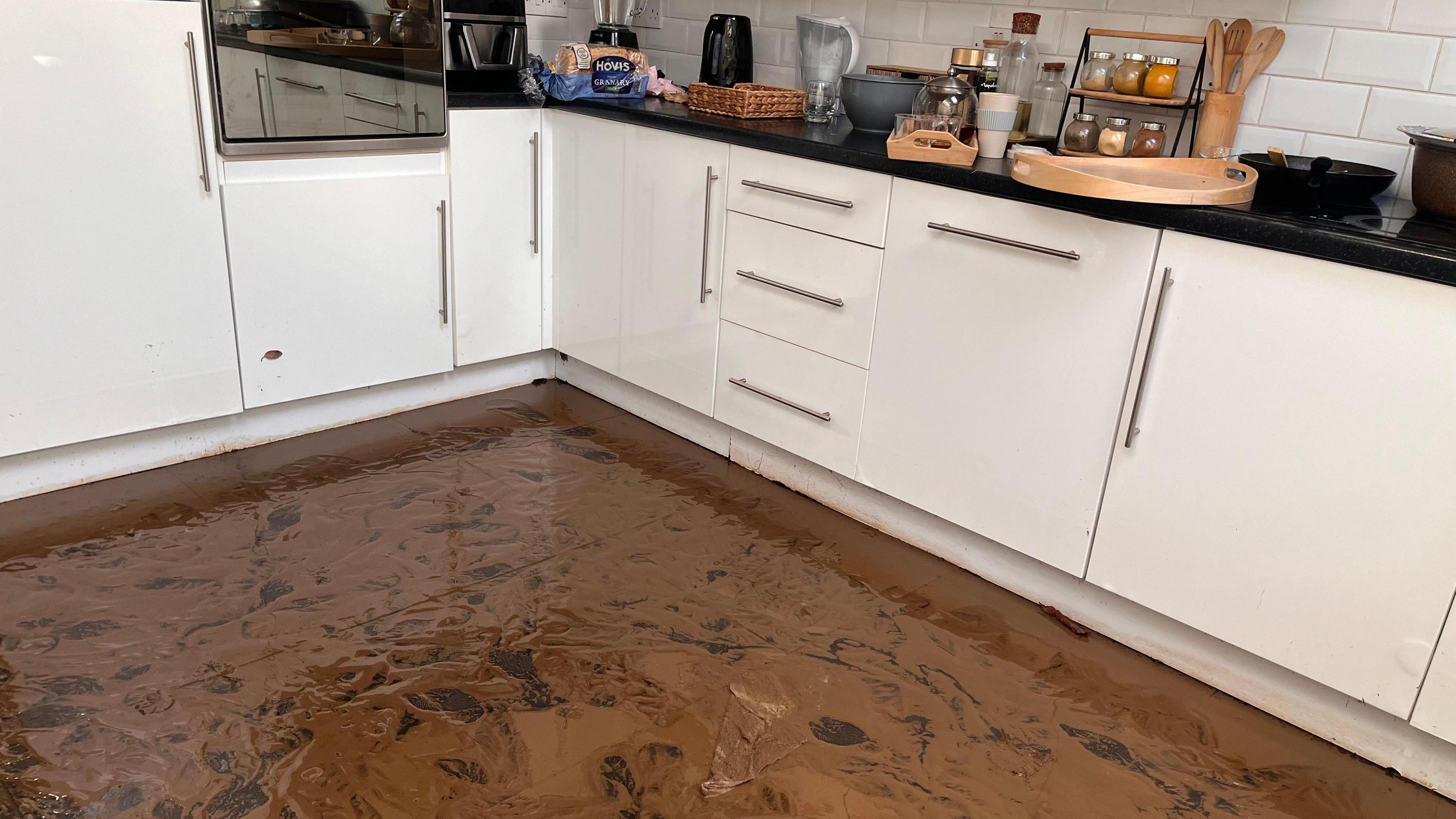 The floor of Mehdi Mozadeh's kitchen in Park Avenue, Dundonald was covered in flood water and brown mud.  The kitchen has white cupboards and there is kitchen equipment on the worktops.