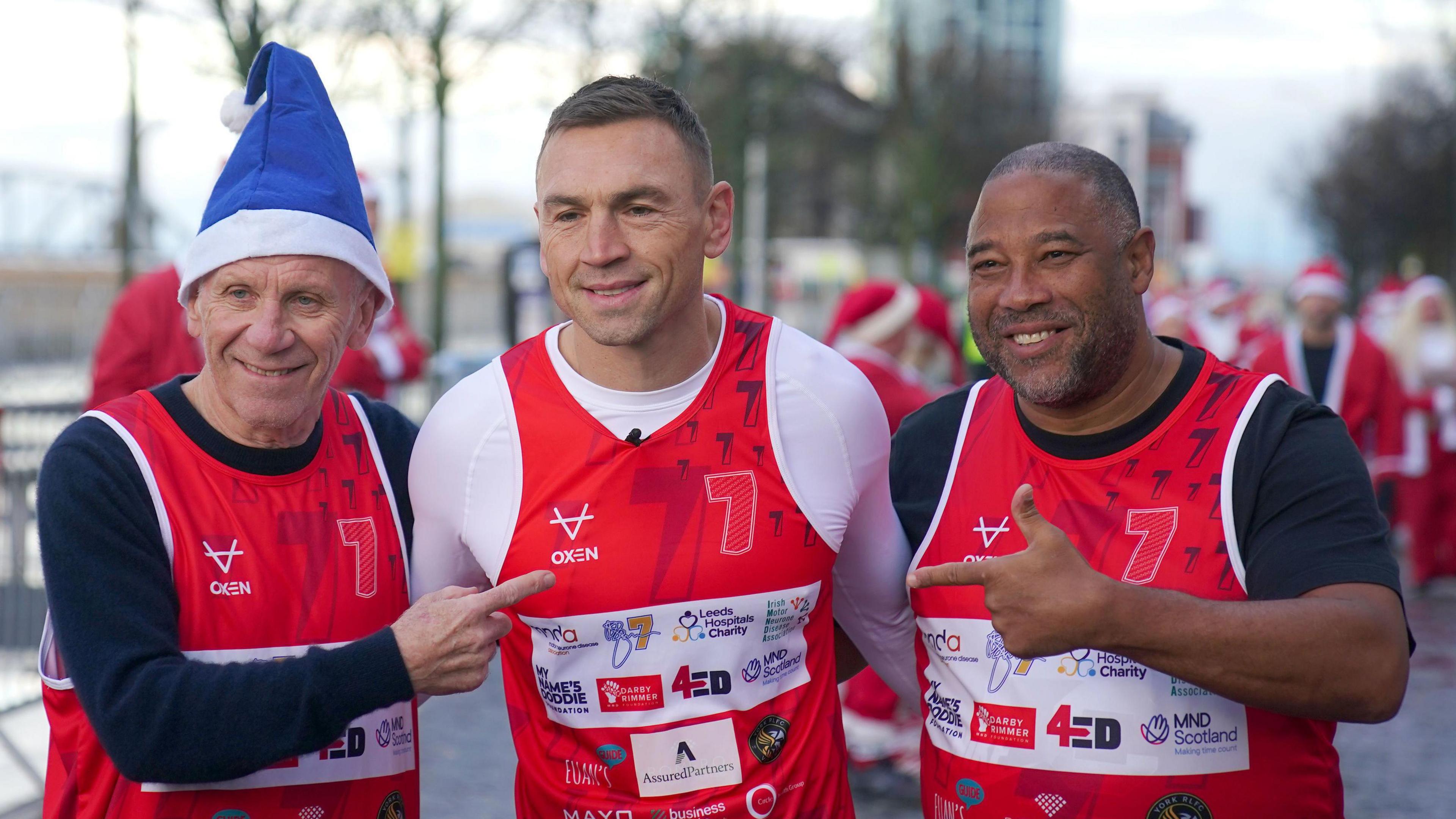 Gorup picture of Peter Reid, wearing an Everton-blue santa hat, and John Barnes pointing to Kevin Sinfield