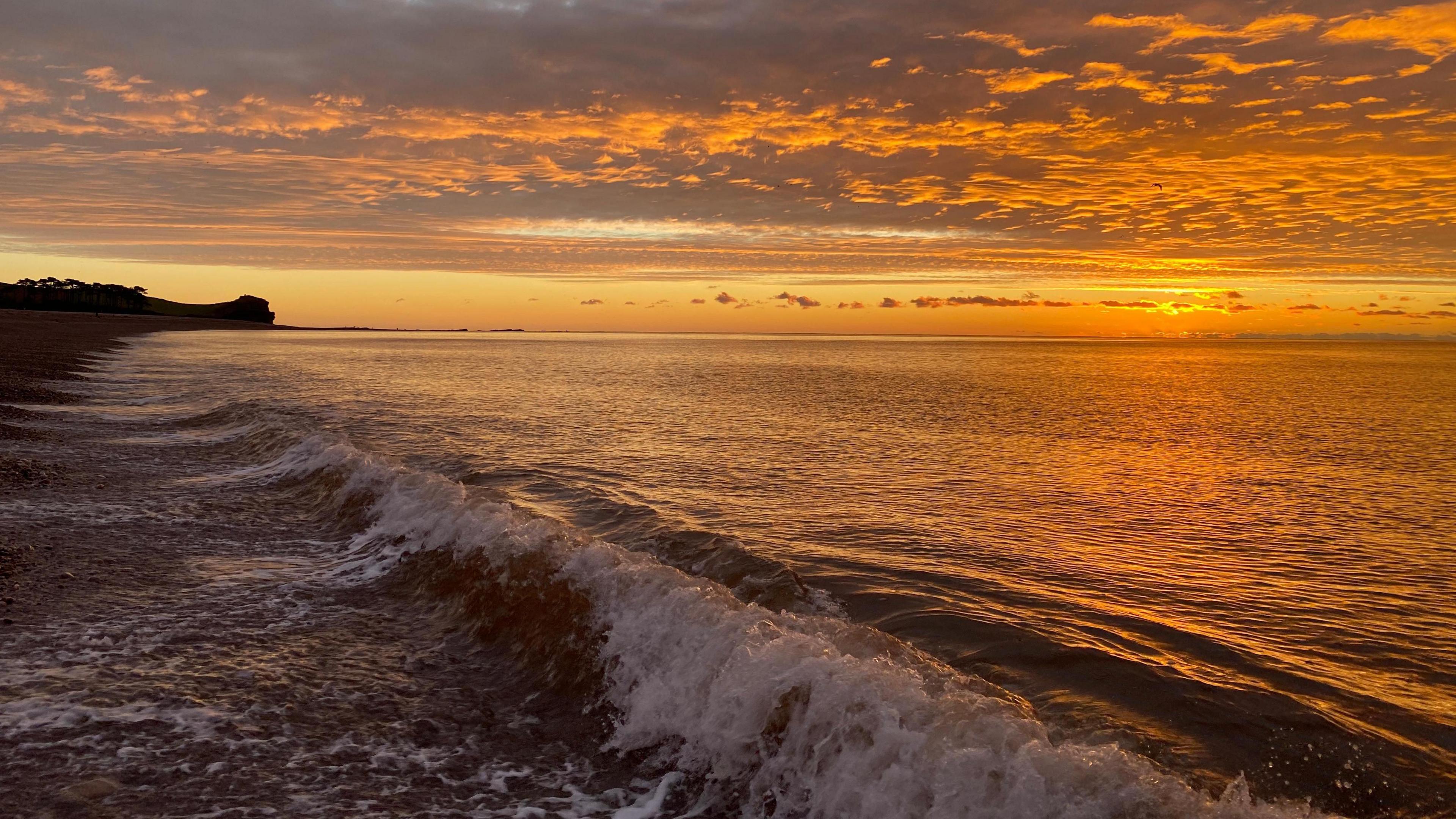 Waves wash onto the beach at Budleigh Salterton on Christmas Day in 2020. The sunrise has left the sky with a hue of orange.