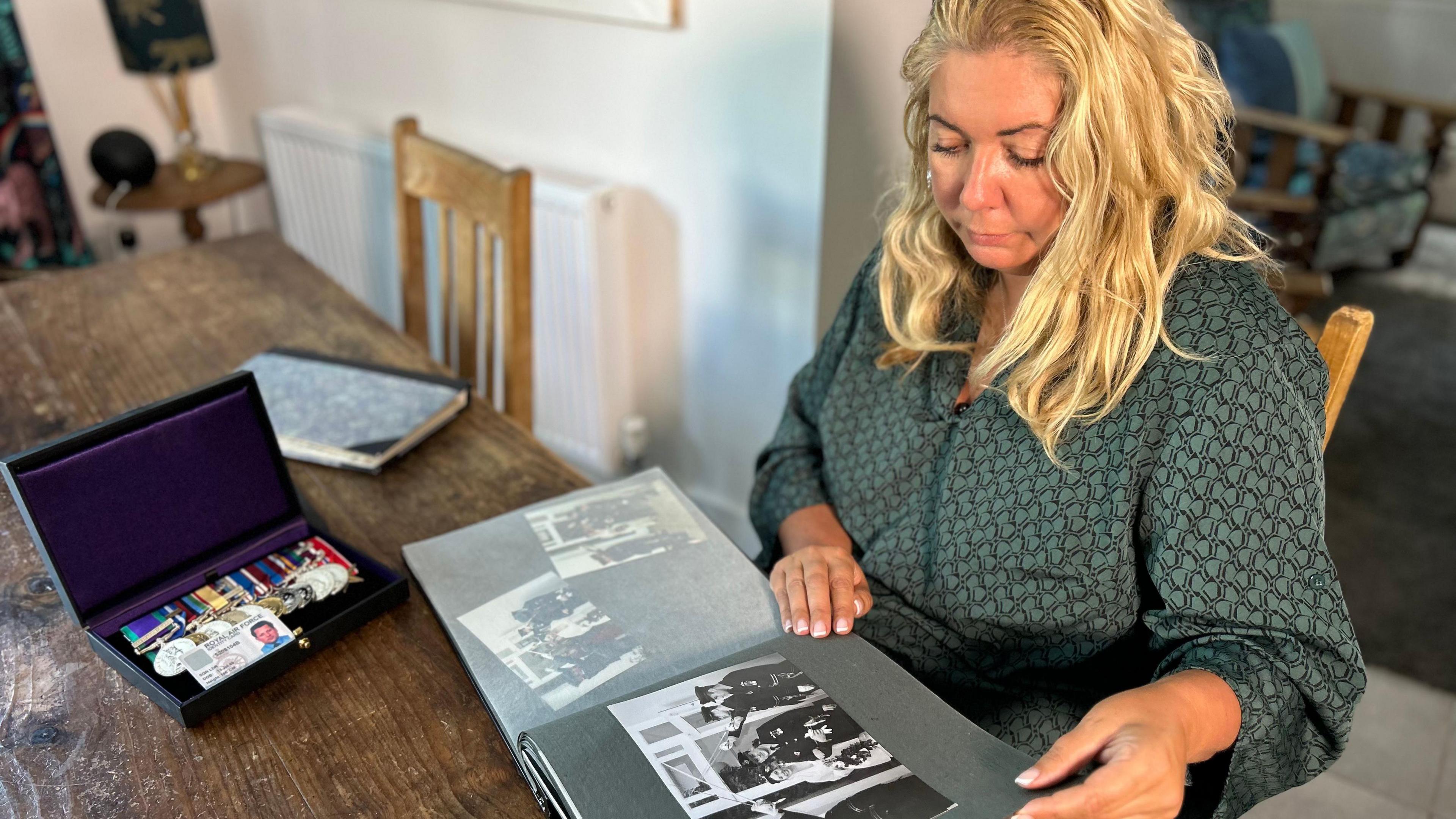 Image of Clare Macnaughton looking at photos of her late husband. His medals are on the table next to her.