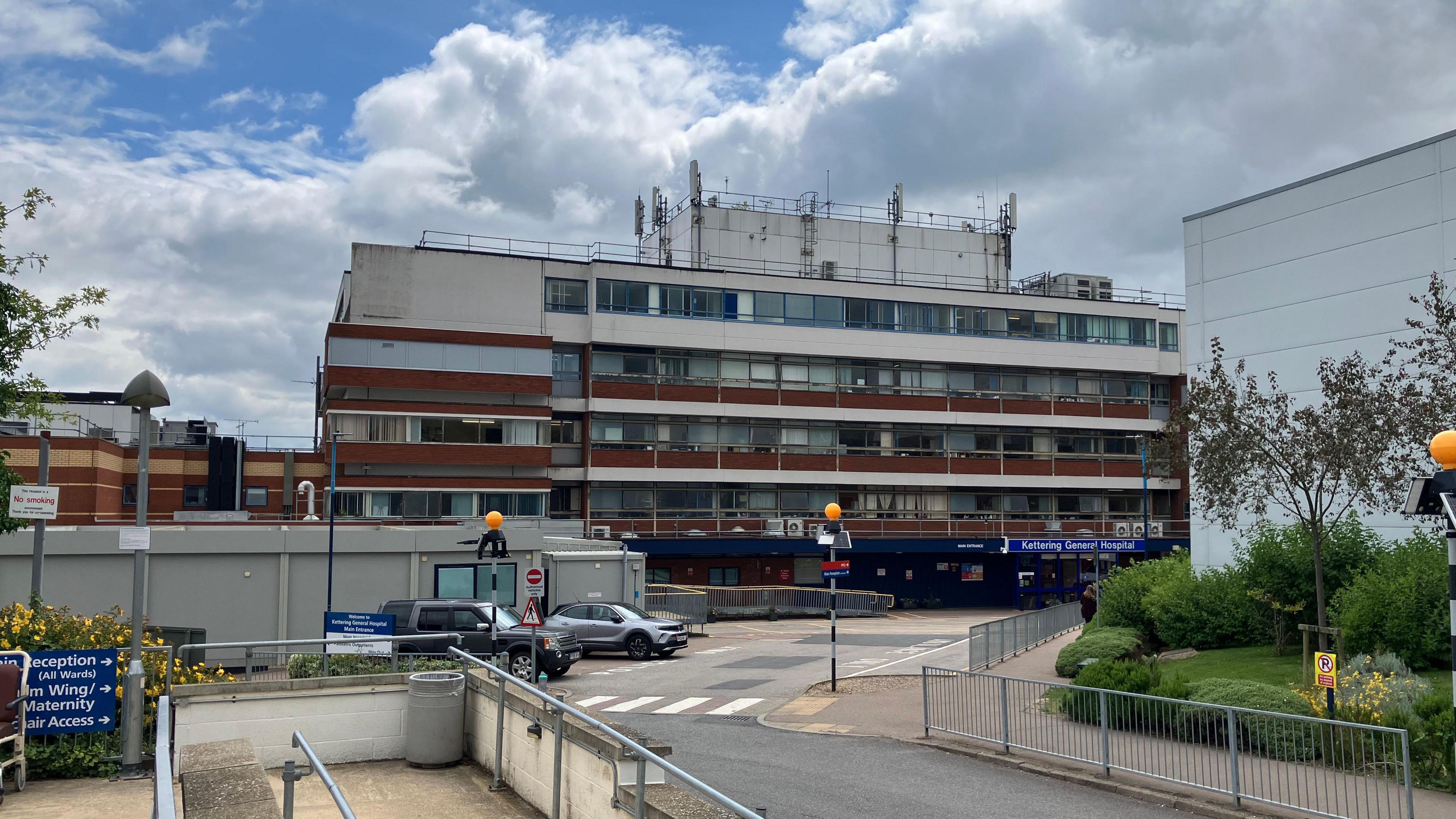 The outside of a five storey building with white and brown panelling with a zebra crossing outside the entrance. 