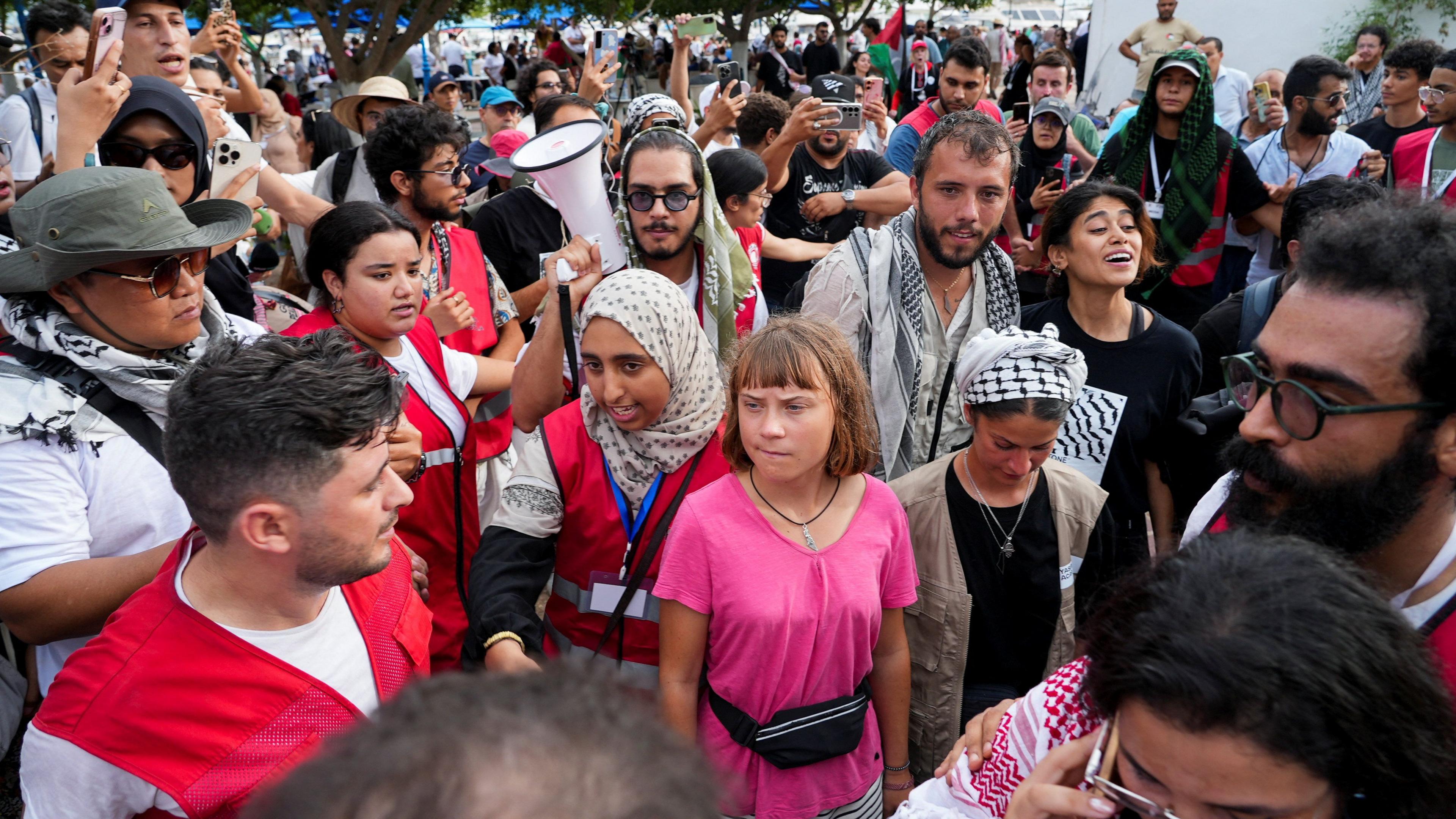Crowds of people, wearing red hi-vis jackets and traditional scarves associated with the pro-Palestine movement surround Greta Thunberg at port Sidi Bou Said.