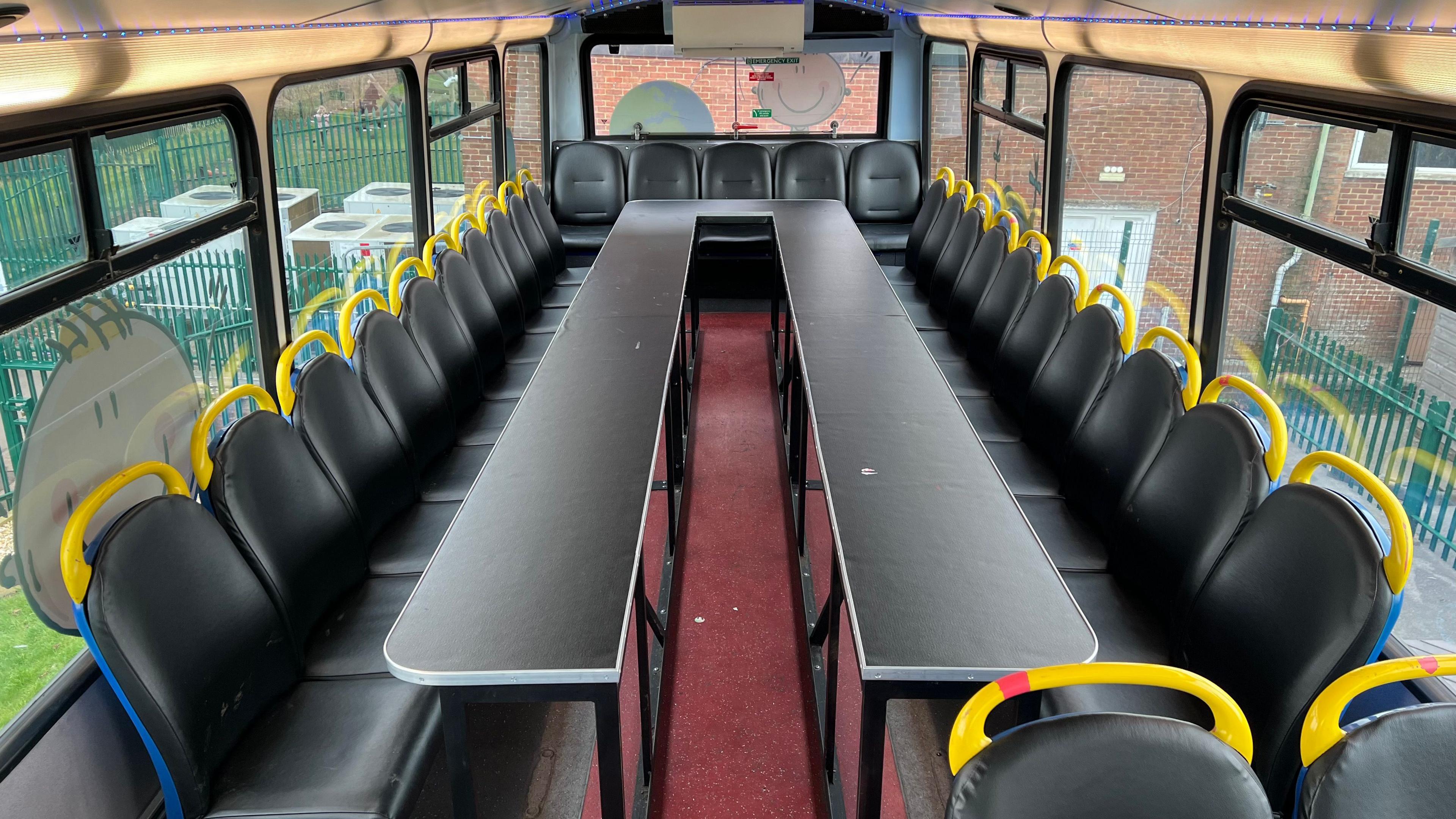 A view of an empty classroom area on the upper deck of the bus. Bus seats have been put around the outside of a long work table.