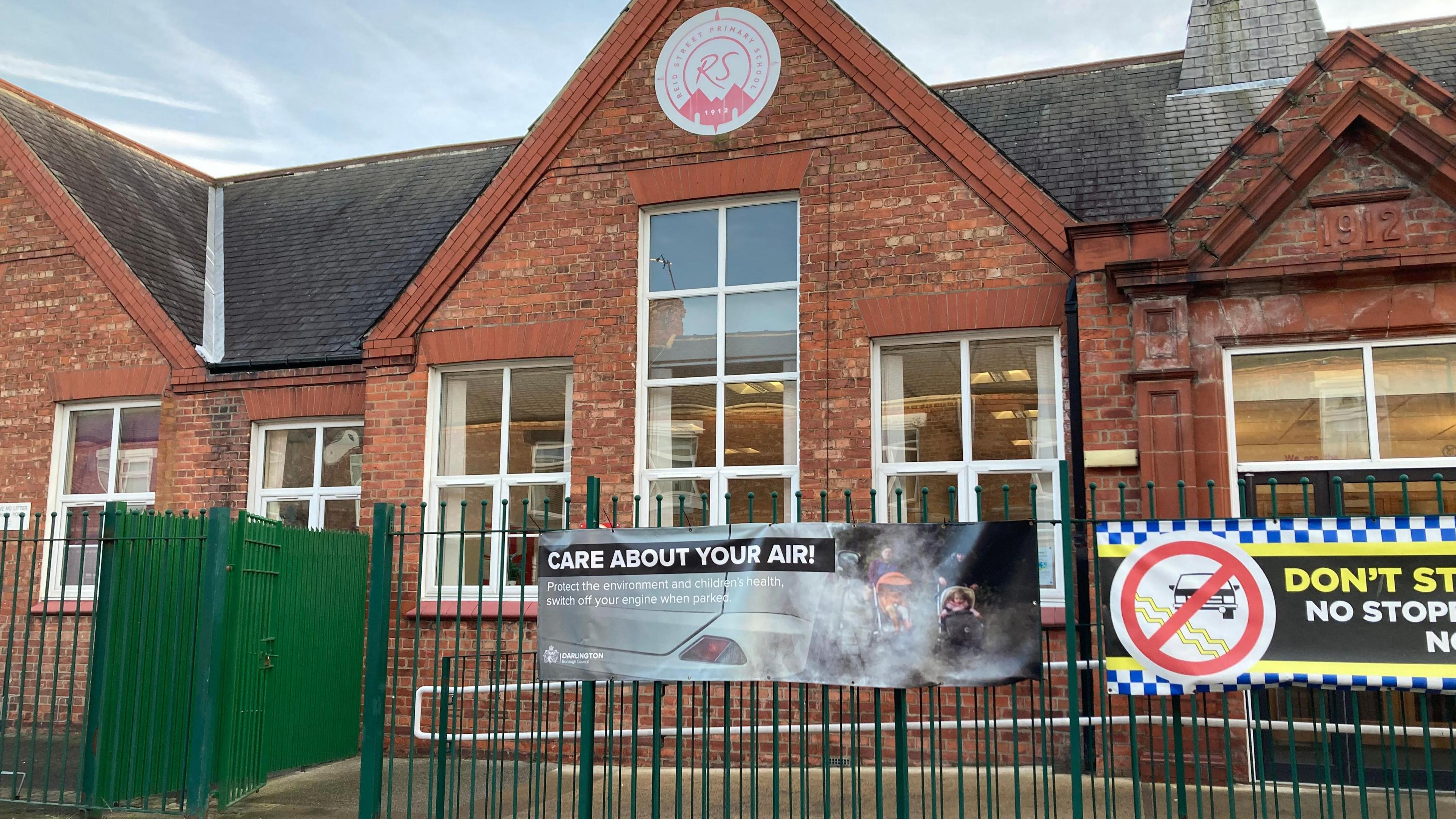 An Edwardian school building with a banner across the school gates reading "Care about your air!"