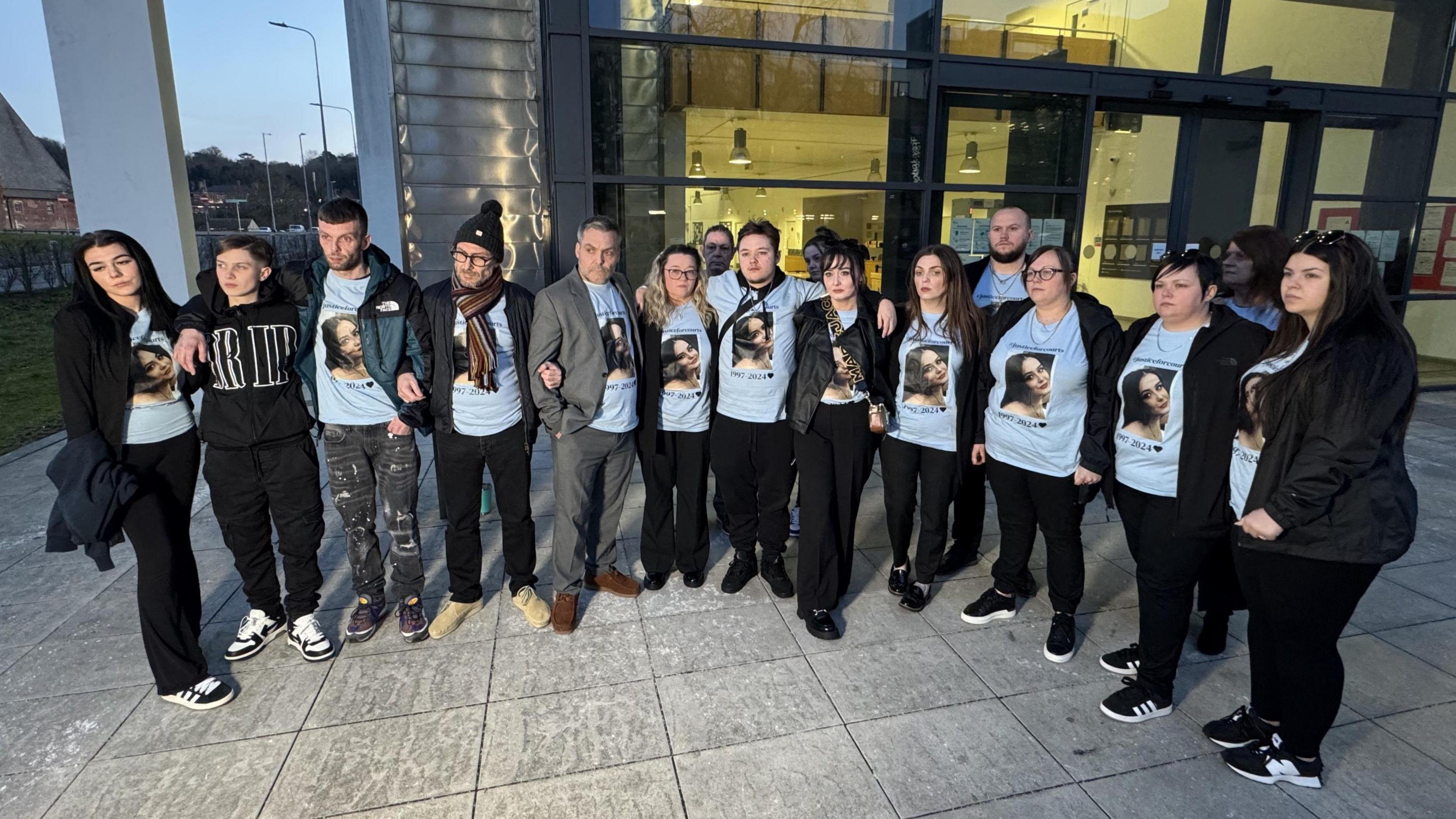 About 14 members of Courtney Mitchell's family standing outside Ipswich Crown Court. They are all wearing blue t-shirts with Ms Mitchell's face printed on them.