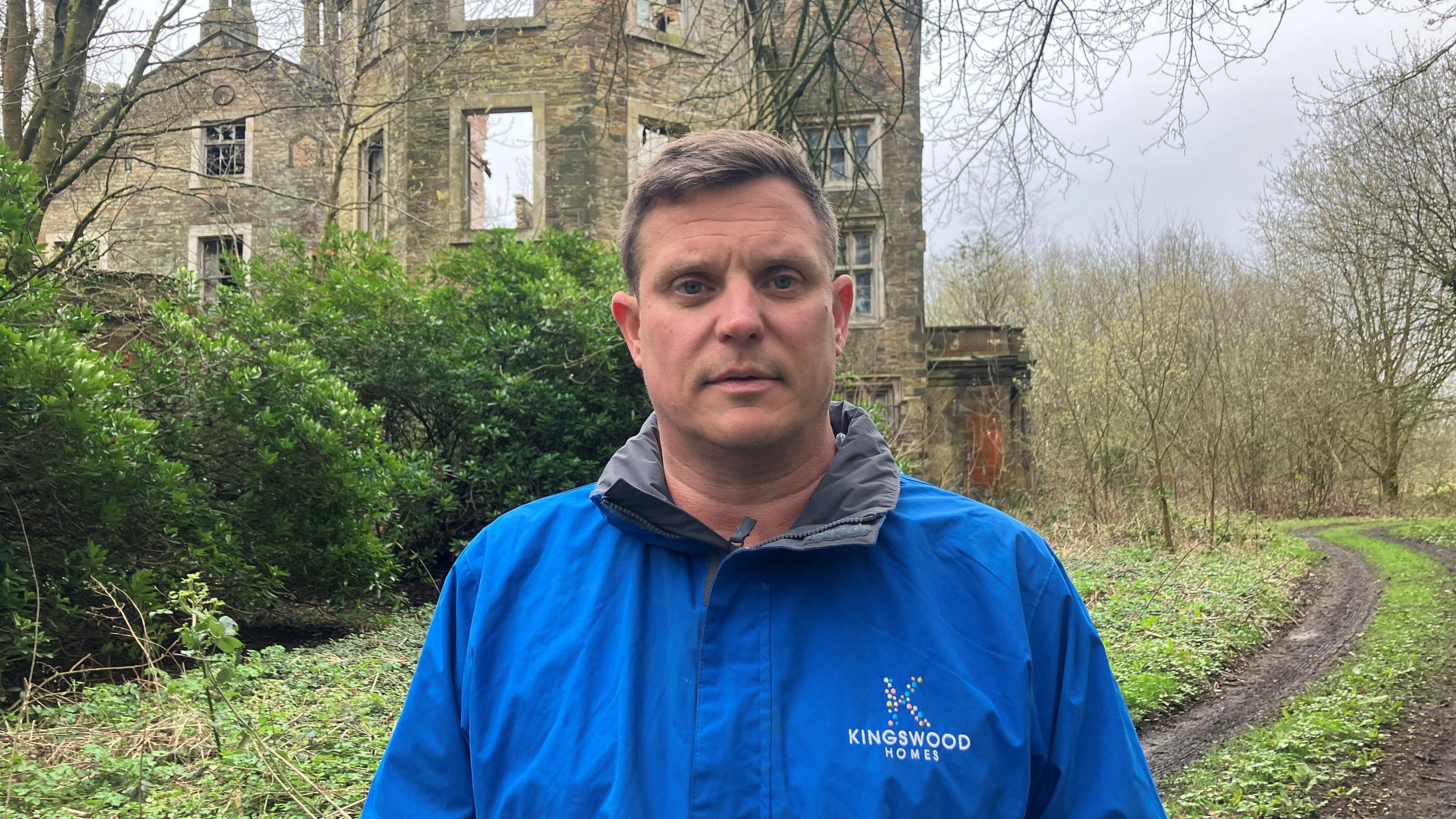 Fotografia e Paul Jones nga Kingswood Homes. Imazhi e tregon atë përpara ndërtesës së rrënuar Winstanley Hall në Wigan. Ai mban veshur një xhaketë shiu blu me logon e kompanisë së tij në pjesën e përparme.