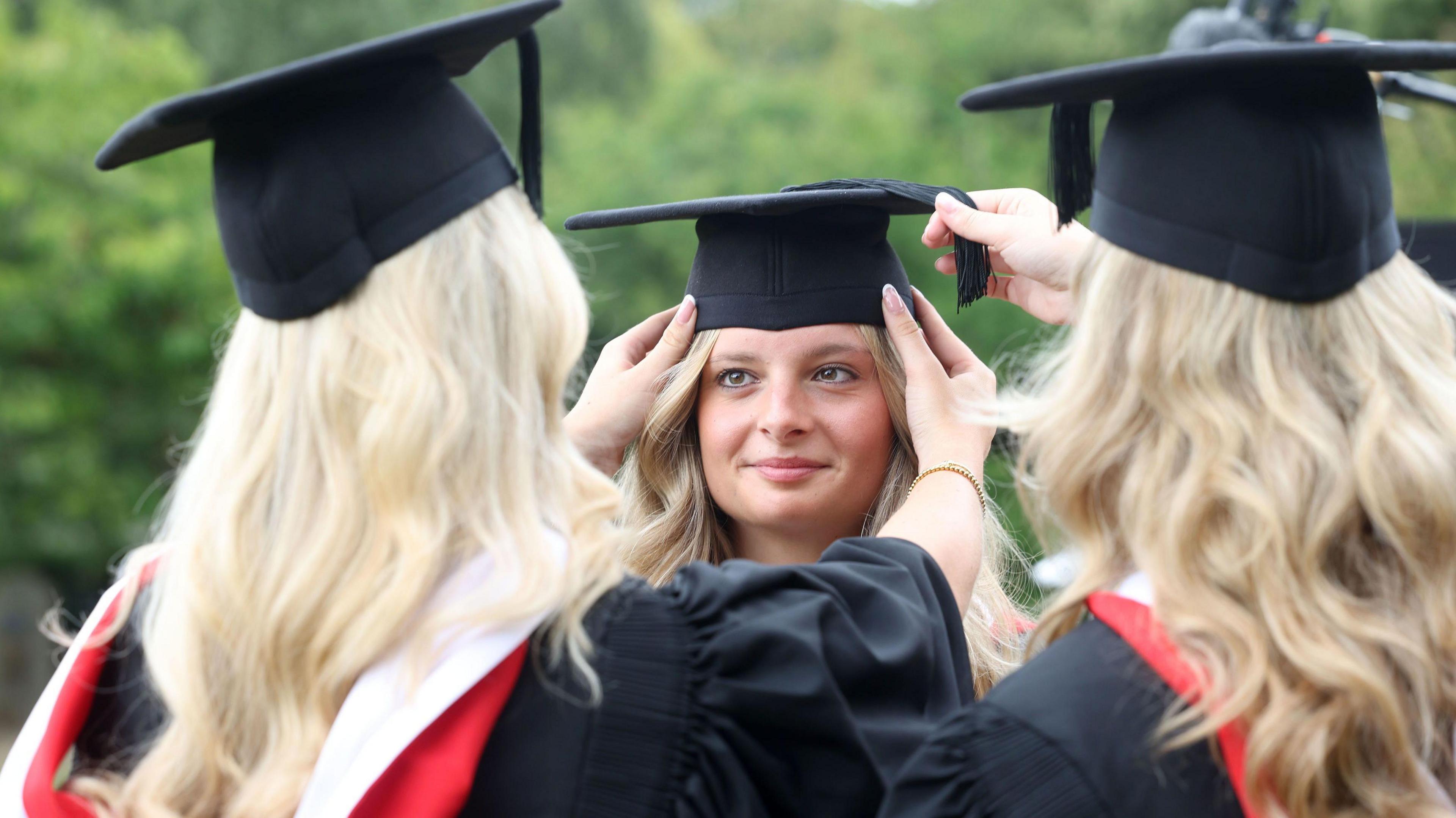 Two of the triplets facing away from the camera as they fix the hair and cap of their sister, who smiles lovingly back at them.