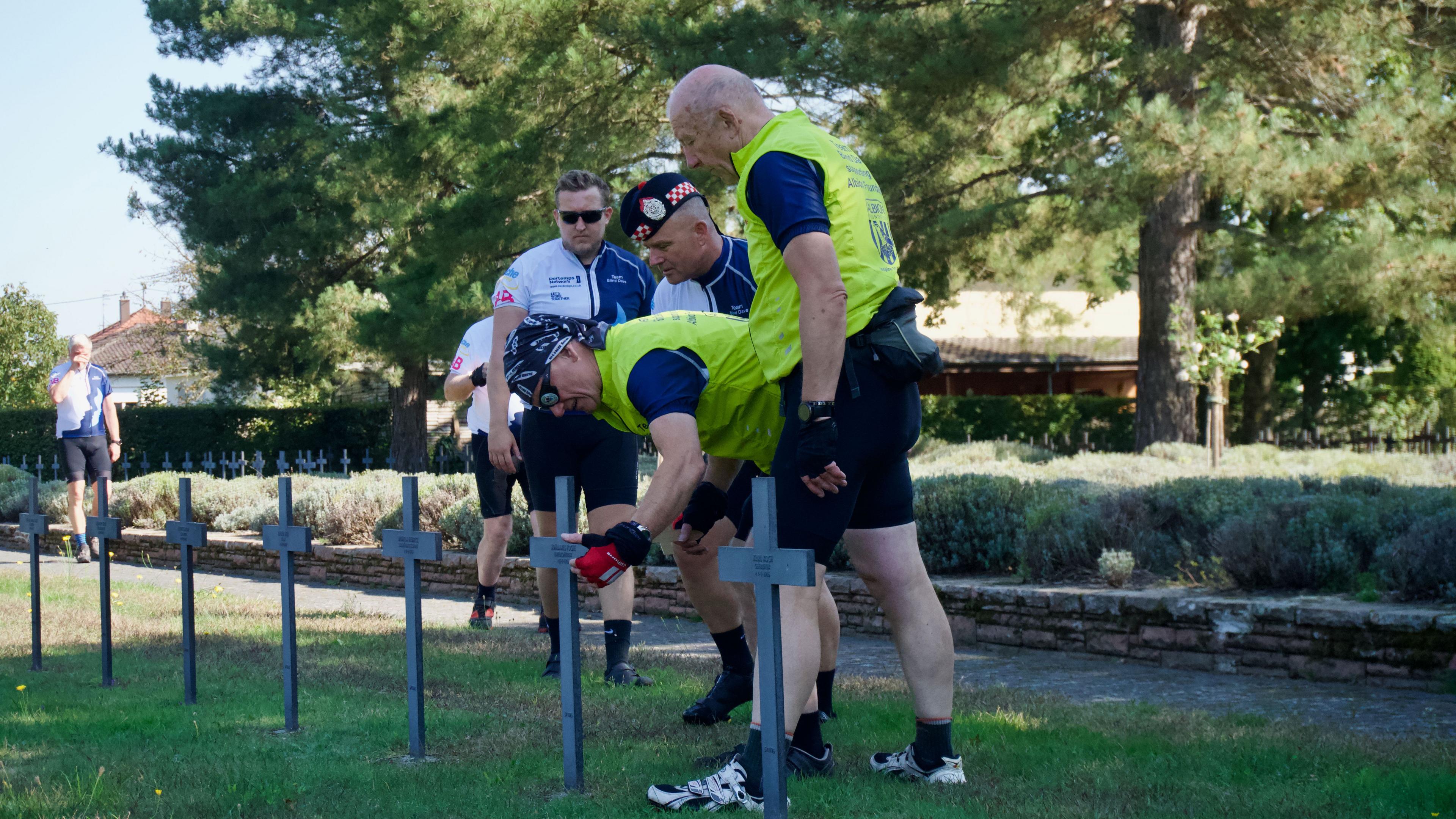 Three men looking at a metal cross in a cemetery