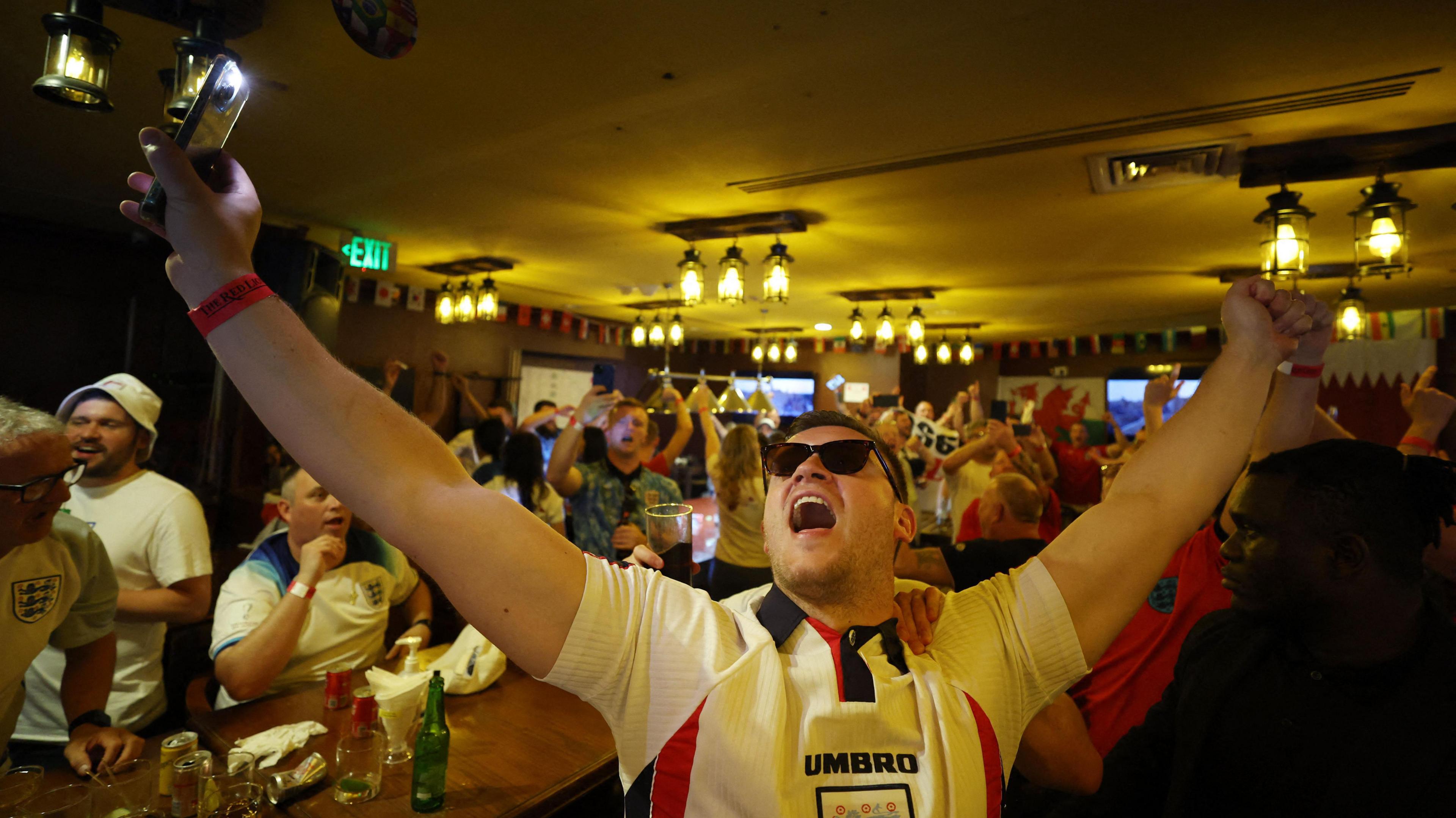 An England football fan celebrates while watching a game at a pub.