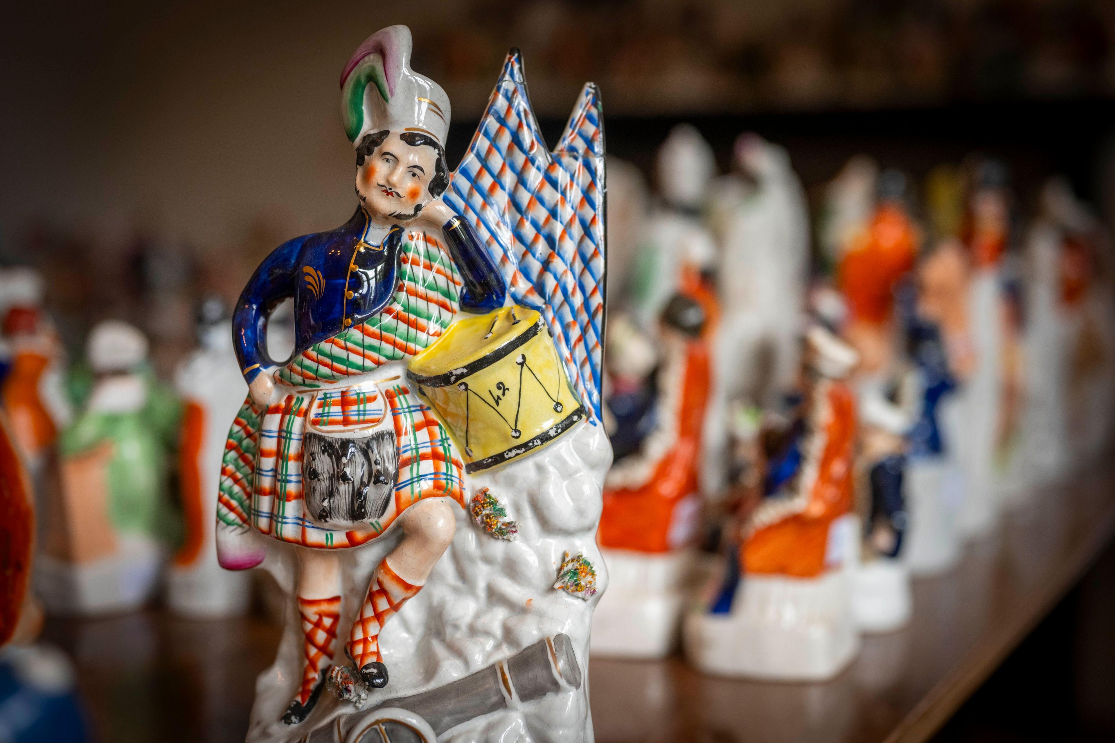 A ceramic Highland soldier with a drum stands on a cannon in front of  a range of other pottery items