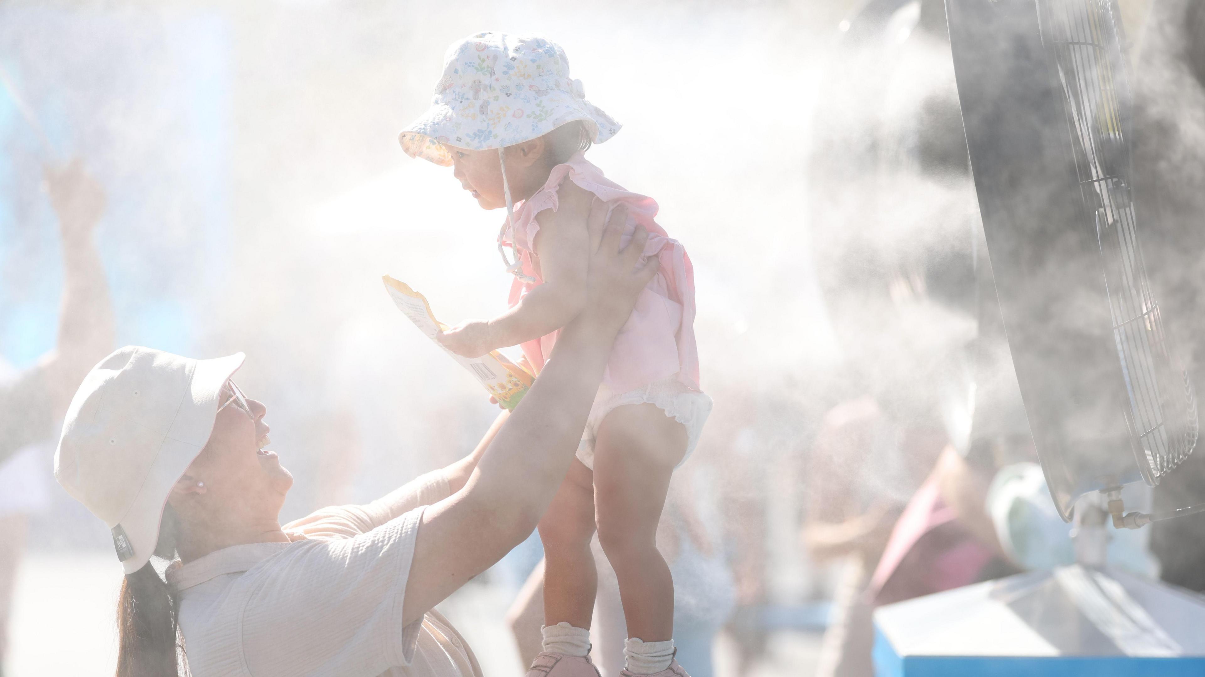 A mother lifts her toddler up in front of a misting machine at Melbourne Park