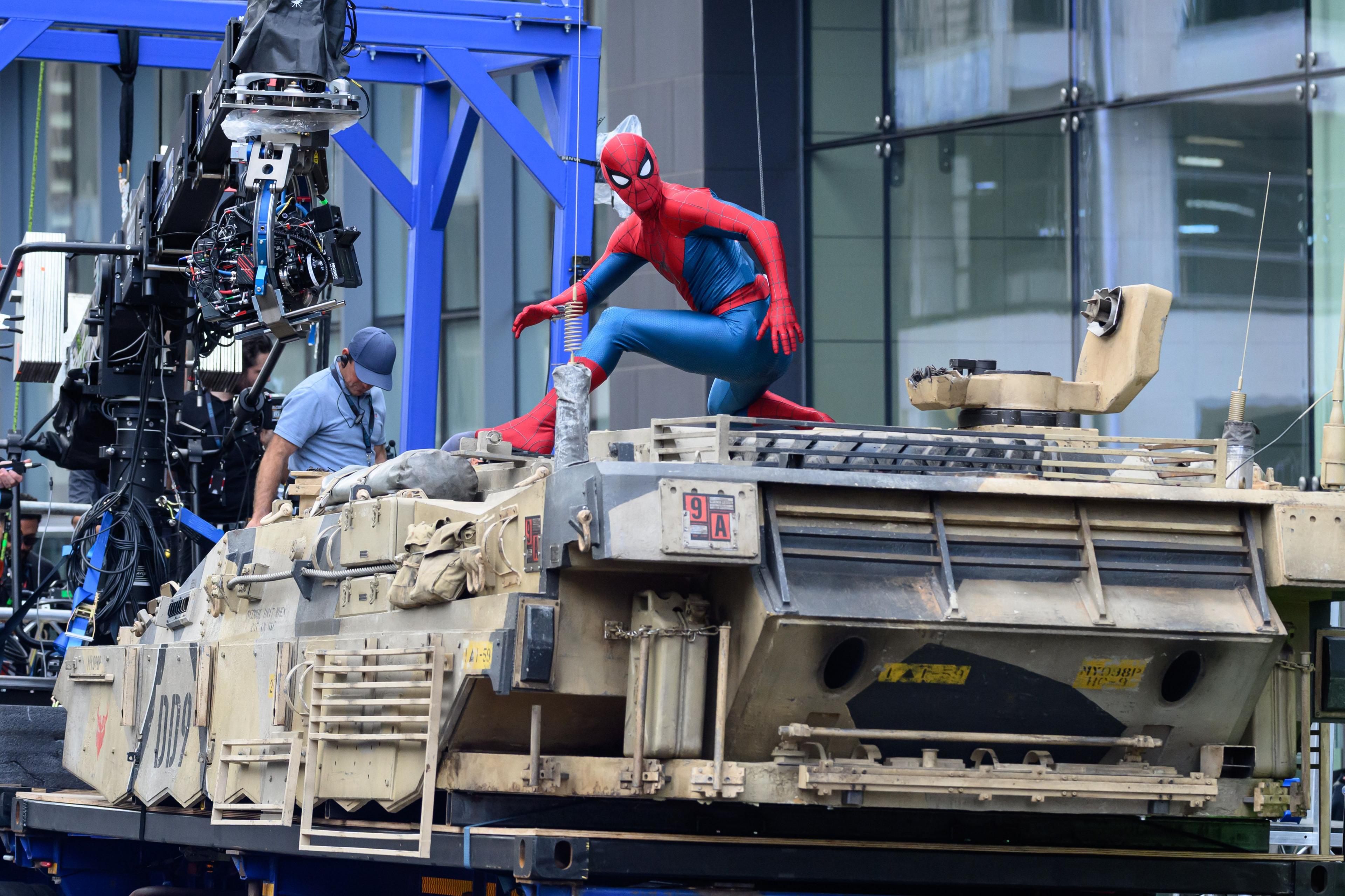 Spider-Man sitting on a tank with a camera crew on the front of it.