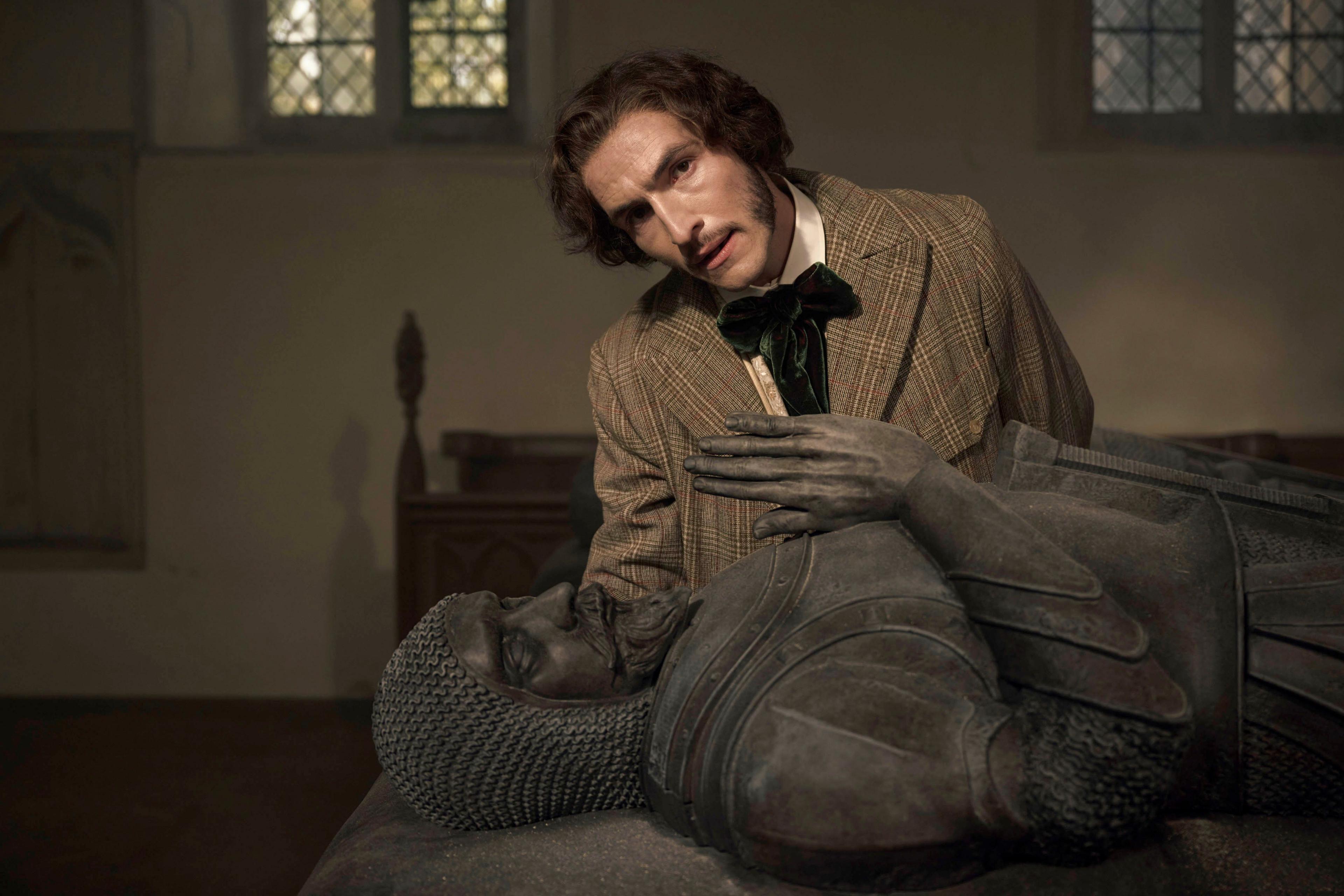 a man in a tweed jacket looks at a stone knight in a church