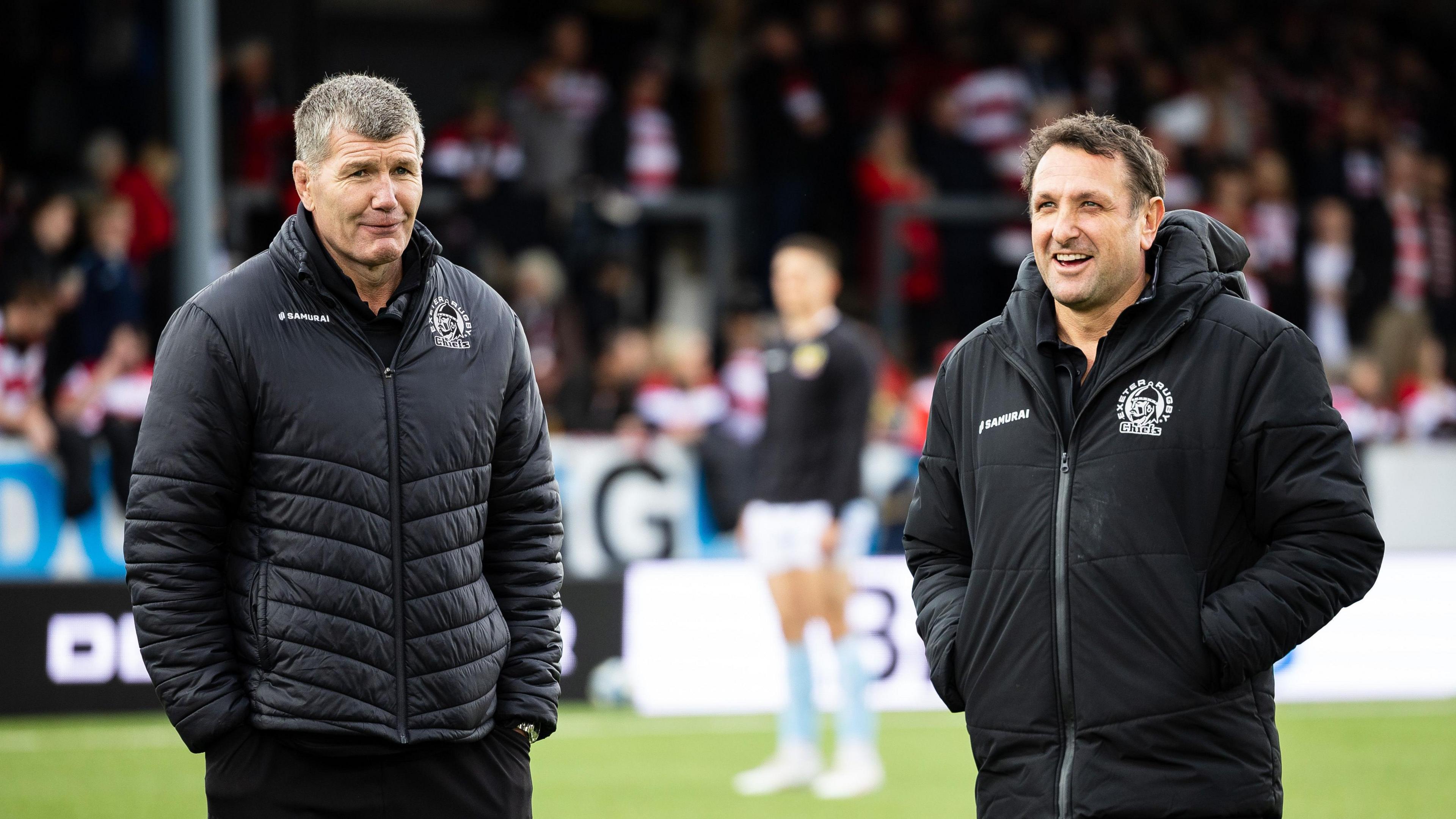 Exeter Chiefs director of rugby Rob Baxter and Ali Hepher both standing with their hands in their pockets.