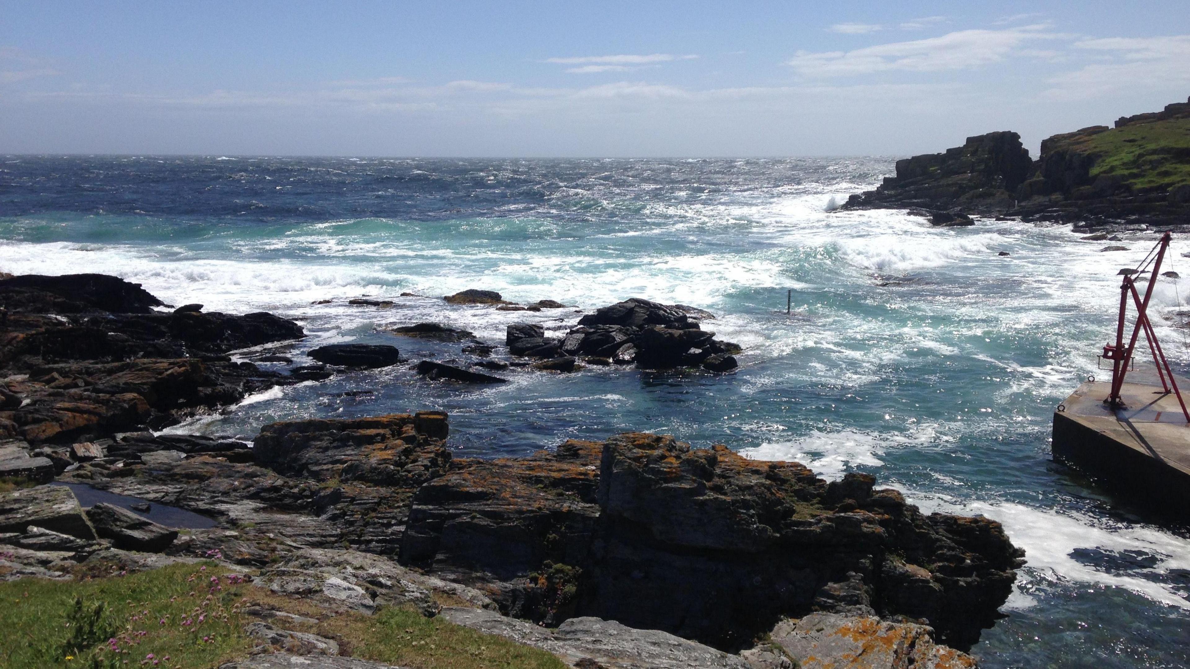 The harbour in the South, with rough seas causing waves to hit against the jagged shoreline.