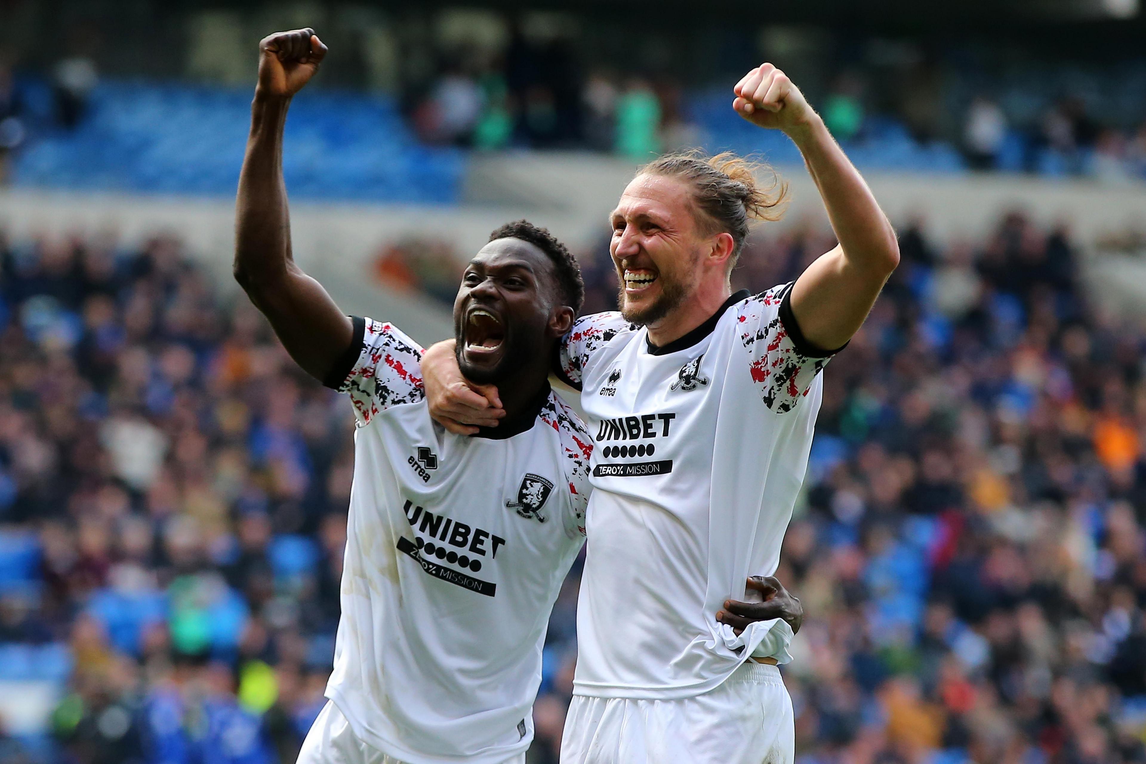 Two players all in white kits hold each other by the waist and hold their arms up in celebration.