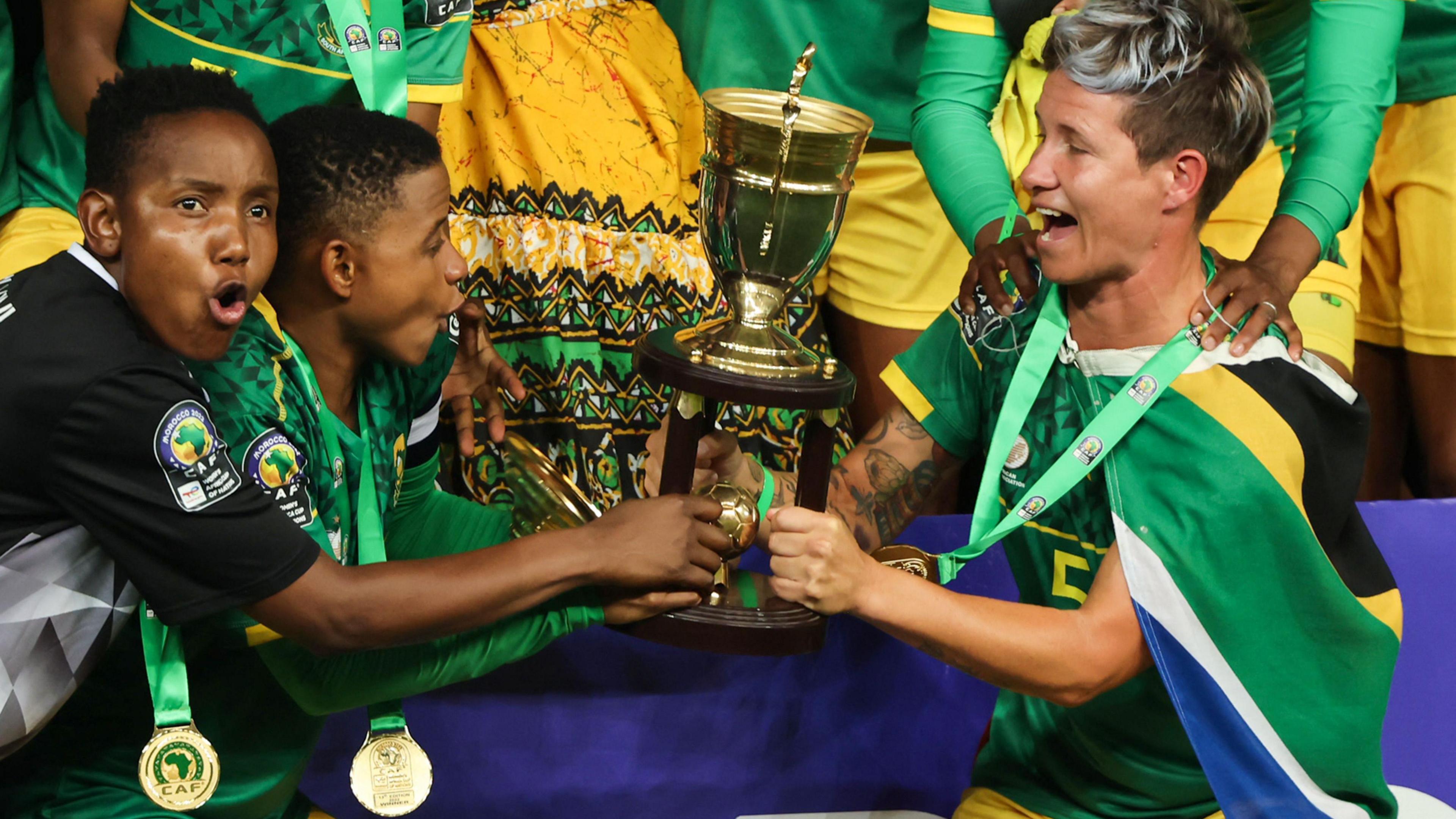 South African players, with medals around their necks on green ribbons, celebrate with the Women's Africa Cup of Nations trophy in 2022