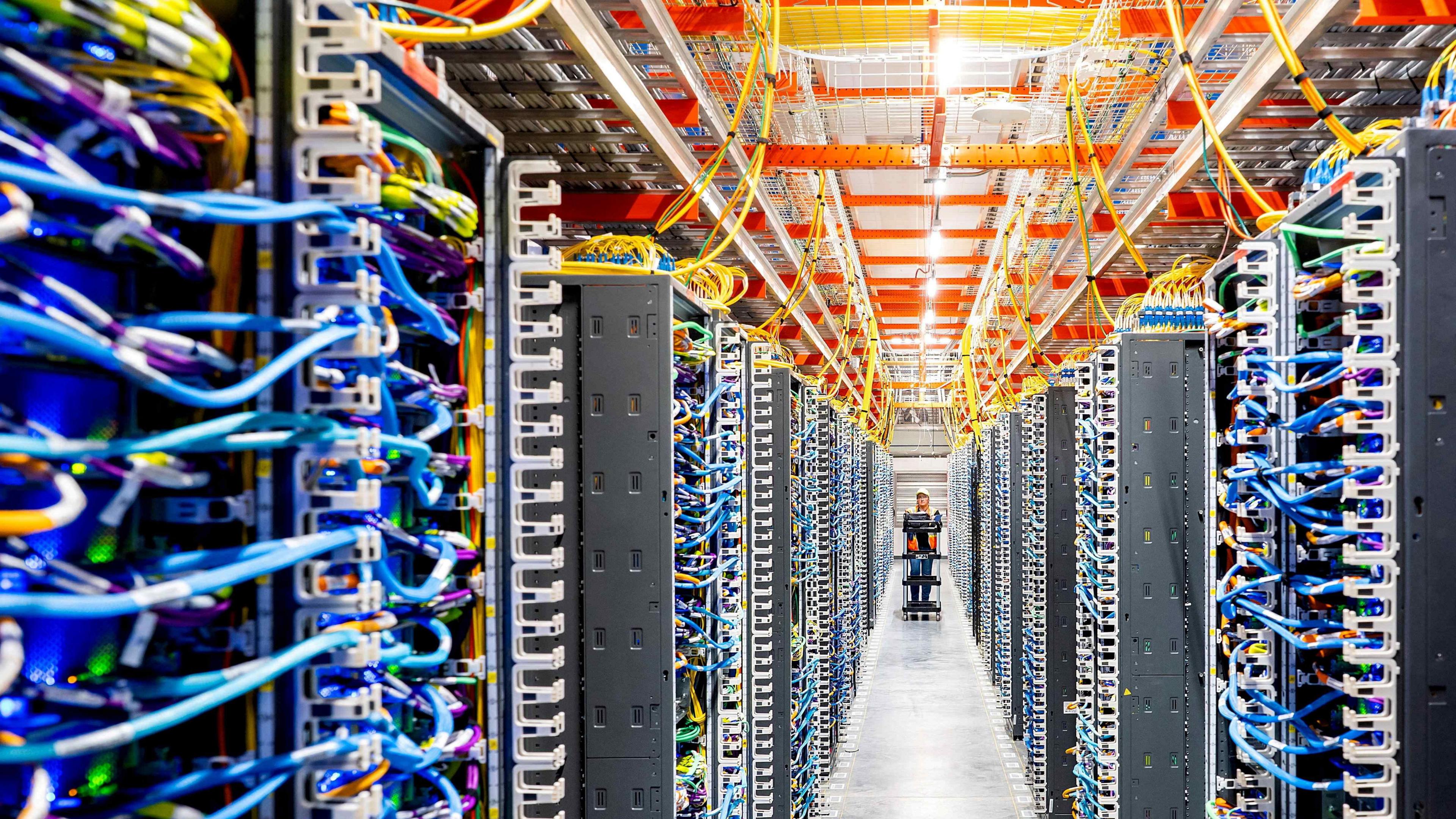 A technician pushing a cart walks through rows of wires inside a data centre.
