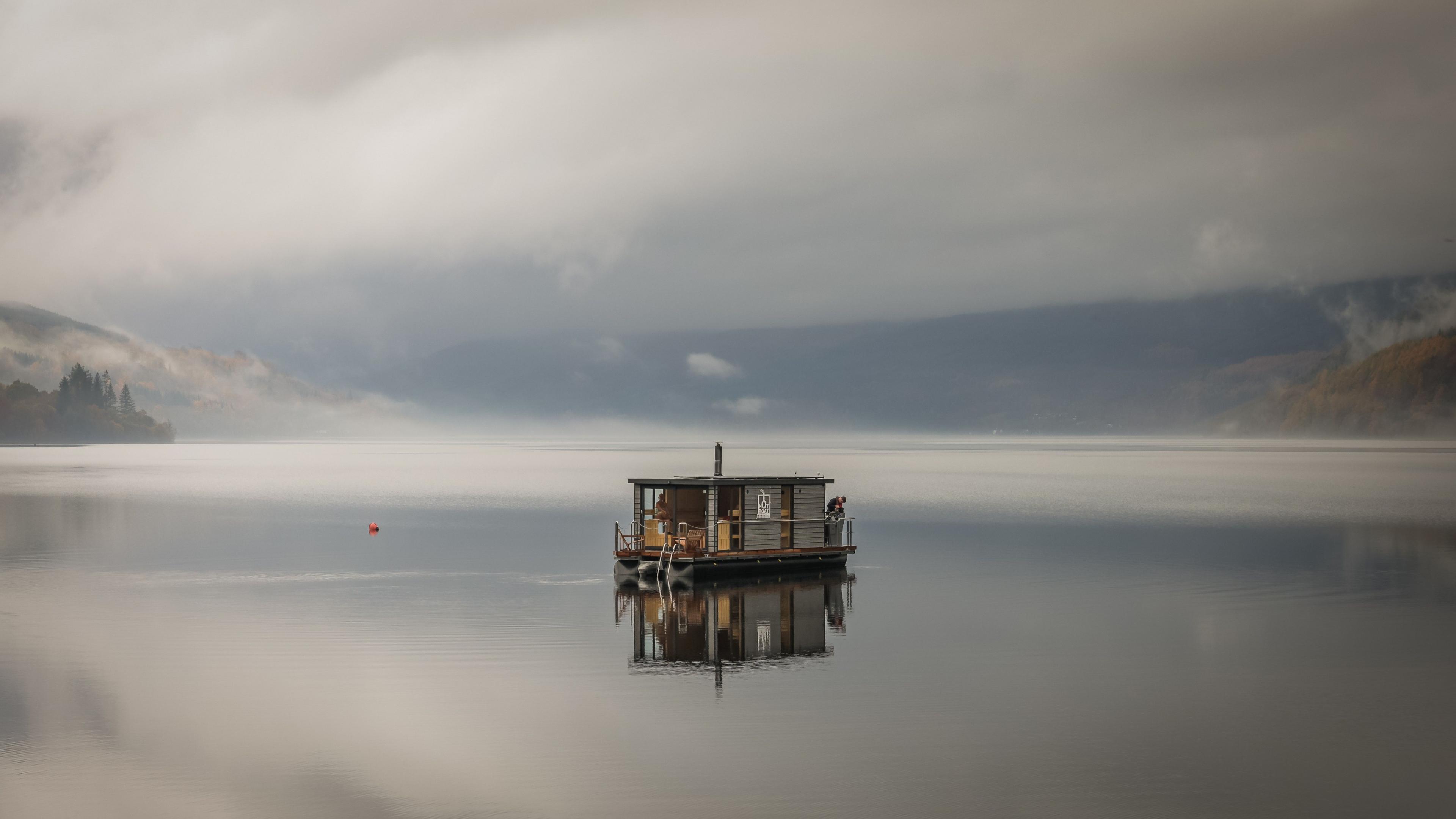 A floating sauna rests on the still heart of Loch Tay. The mist drifts slow across the water, the hills fade into cloud, and the whole glen feels caught between dream and waking.