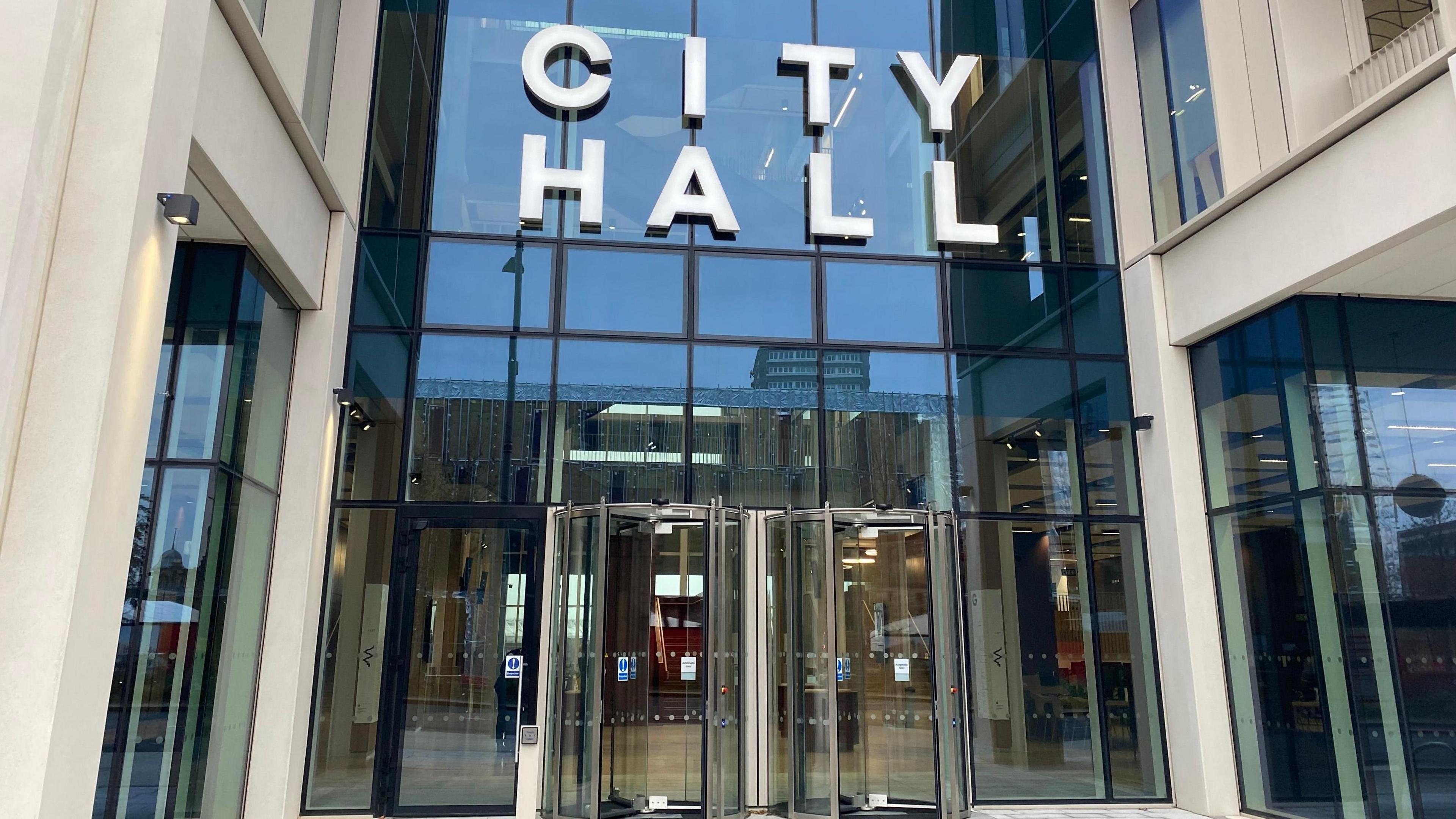 Sunderland City Council's headquarters. The glass fronted building has two revolving doors at its entrance. The words CITY HALL sit above the doors.