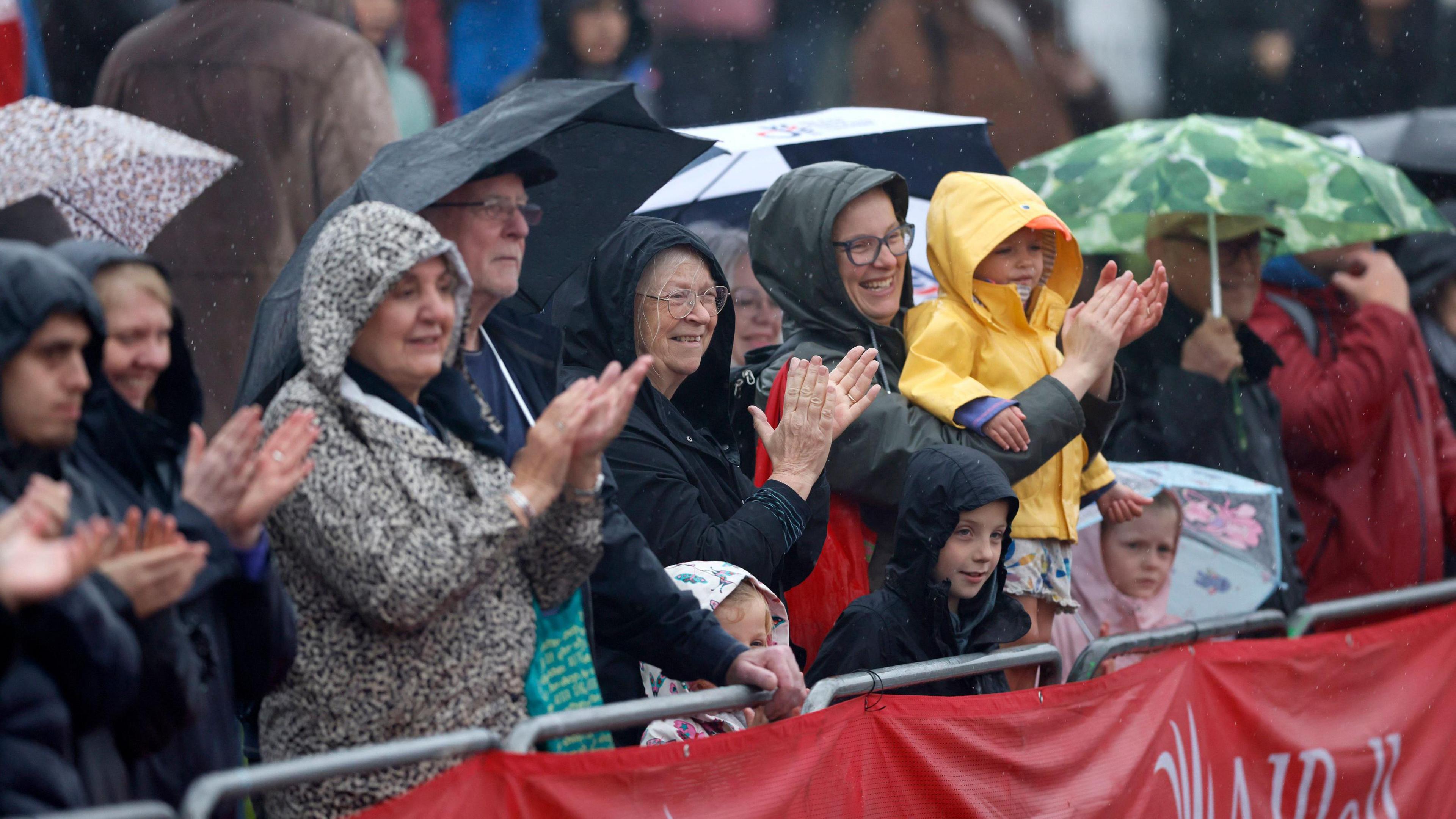 Spectators in wet weather wearing waterproof jackets and carrying umbrellas as they watch the Great North Run.