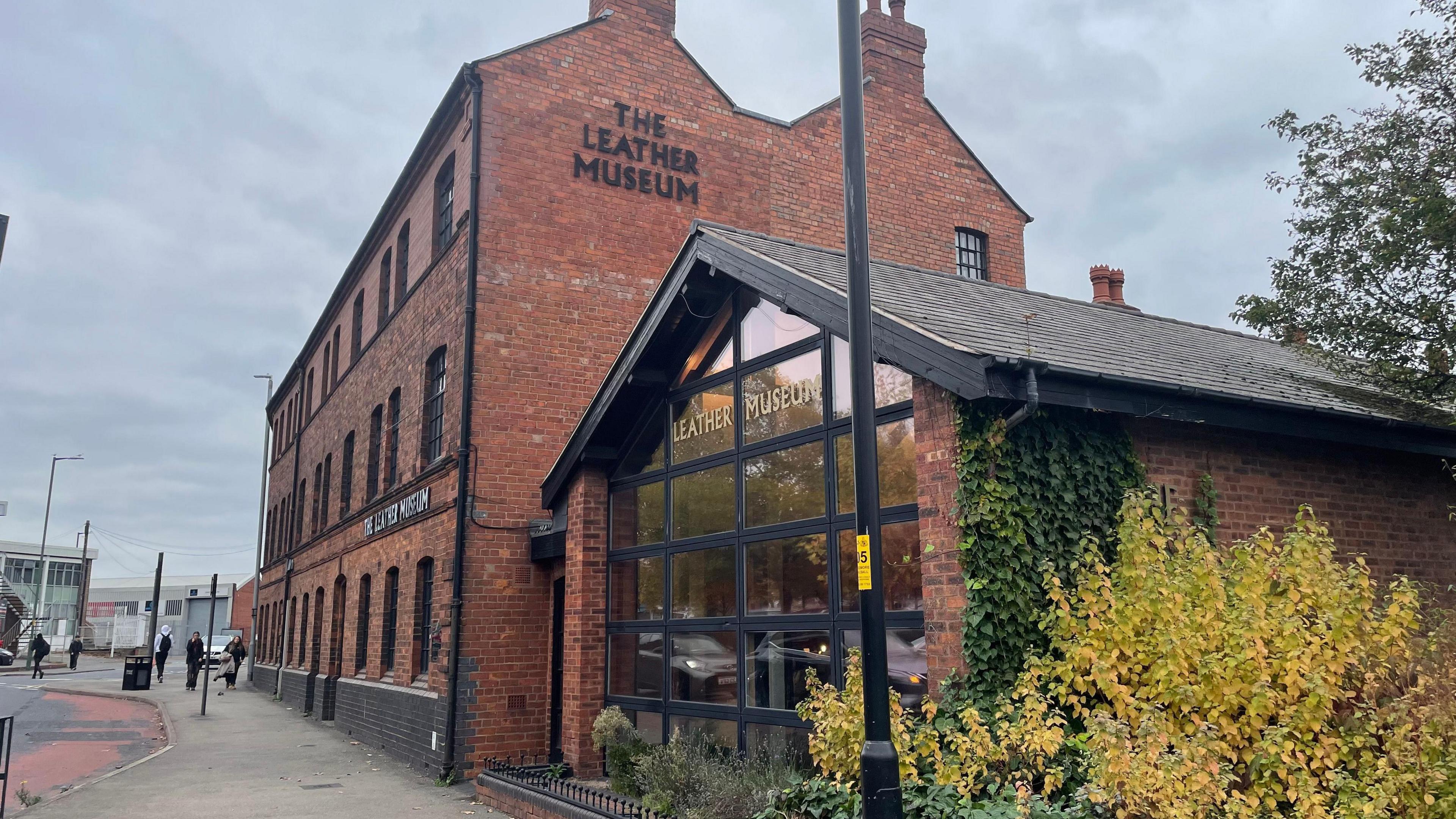 The exterior of a leather museum, showing a red brick building, and a smaller building attached to it with its front wall made completely of glass.