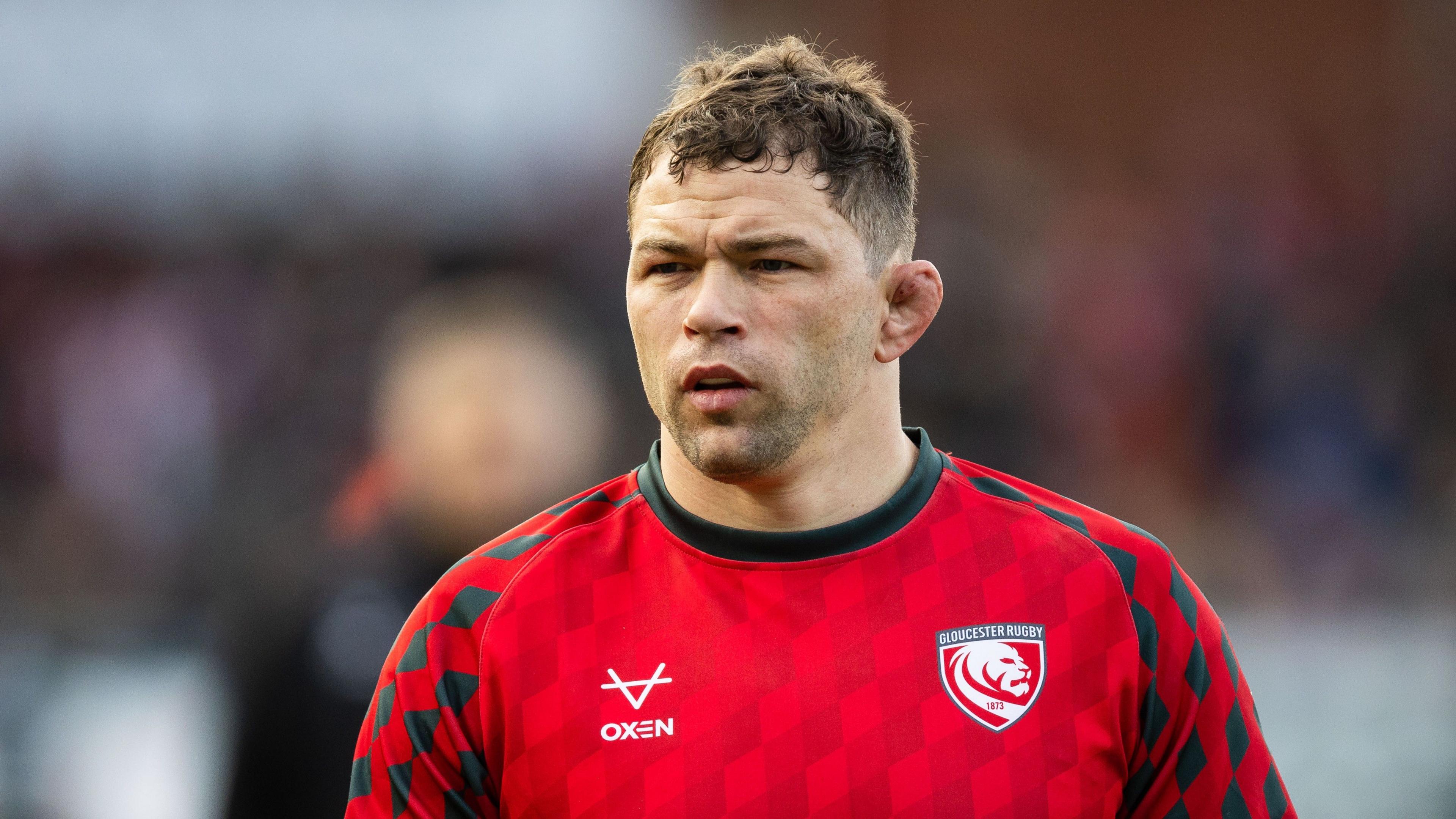 Gloucester rugby player Kirill Gotovtsev looks on in the warm-up for a Premiership Rugby match, wearing a red training top with the team logo on.