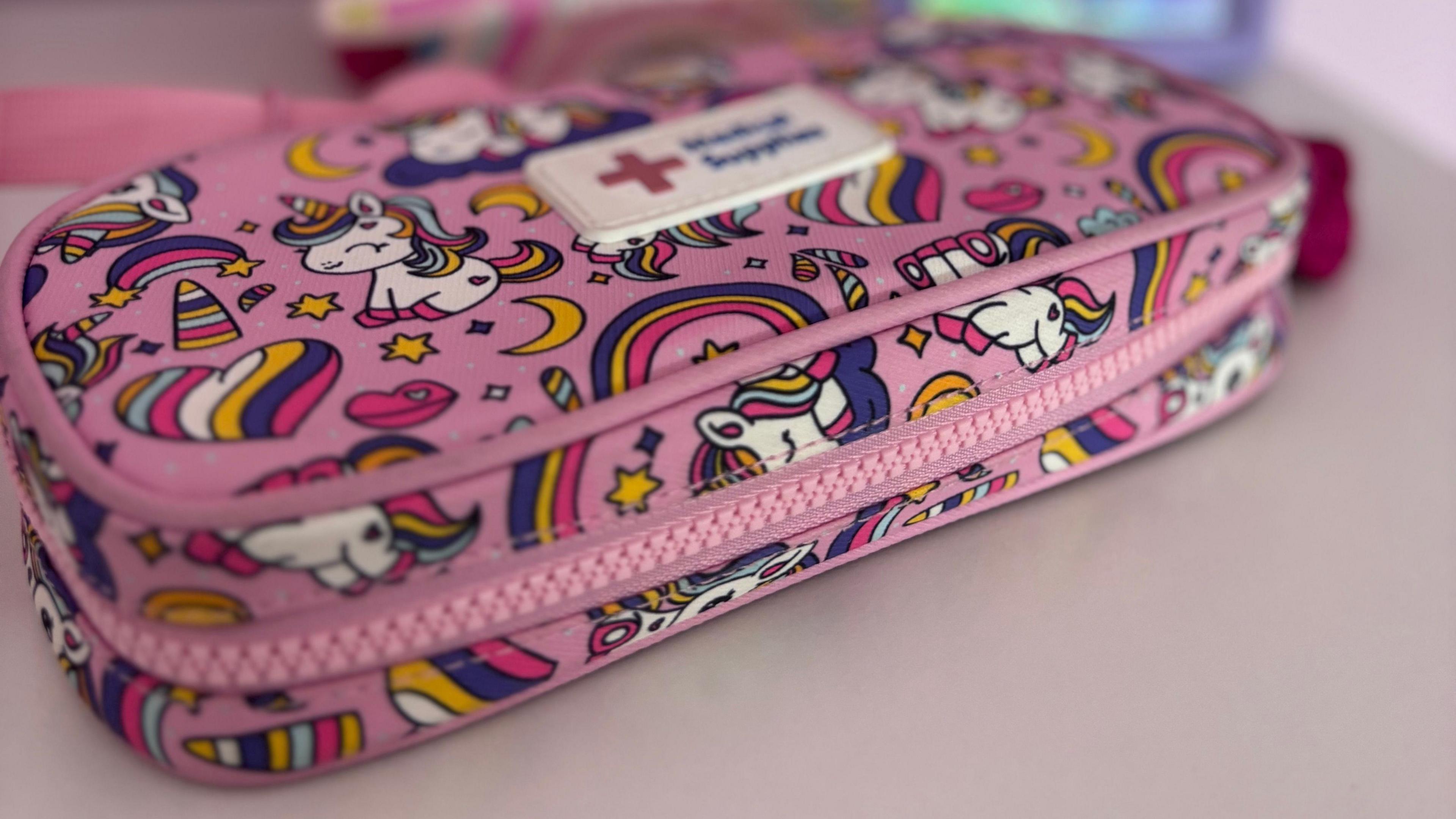A pink case with unicorns on it, showing a medical sign, and a large zip round it.