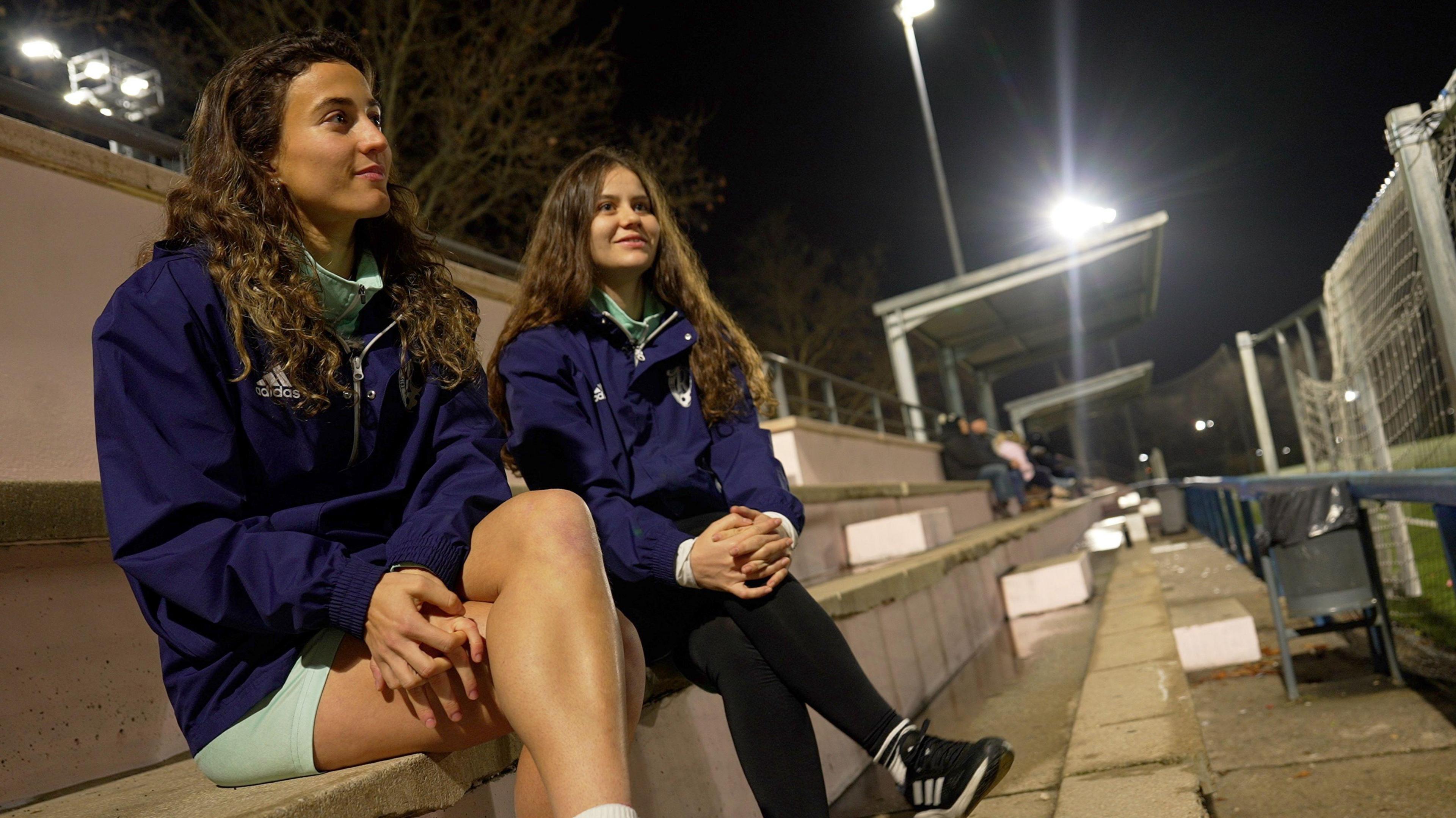 Belén Peralta and Andrea Rodríguez, two young football players, sitting on the stands next to their football pitches. 