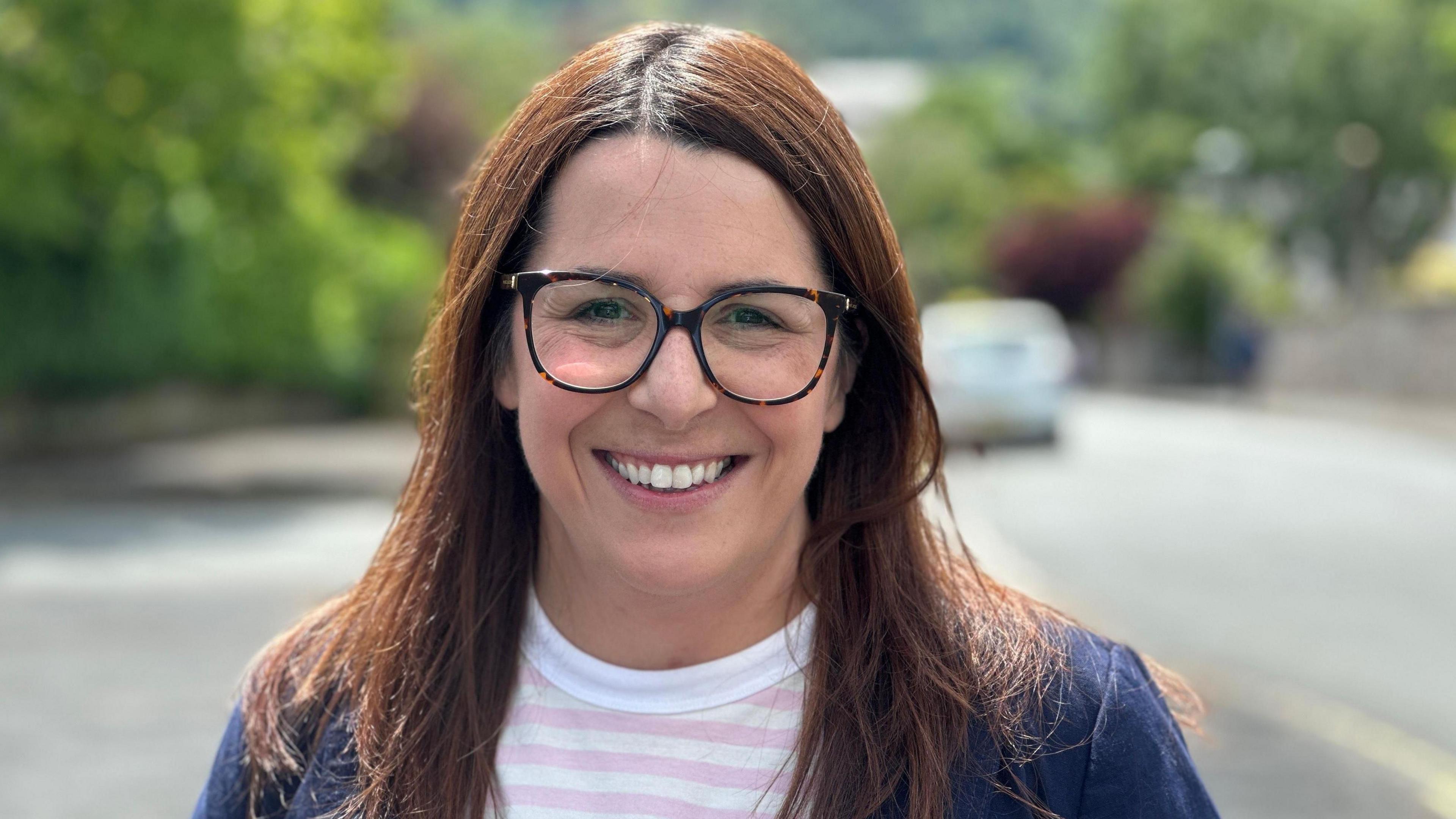 Picture of Fay Jones smiling standing on a street with greenery in the background