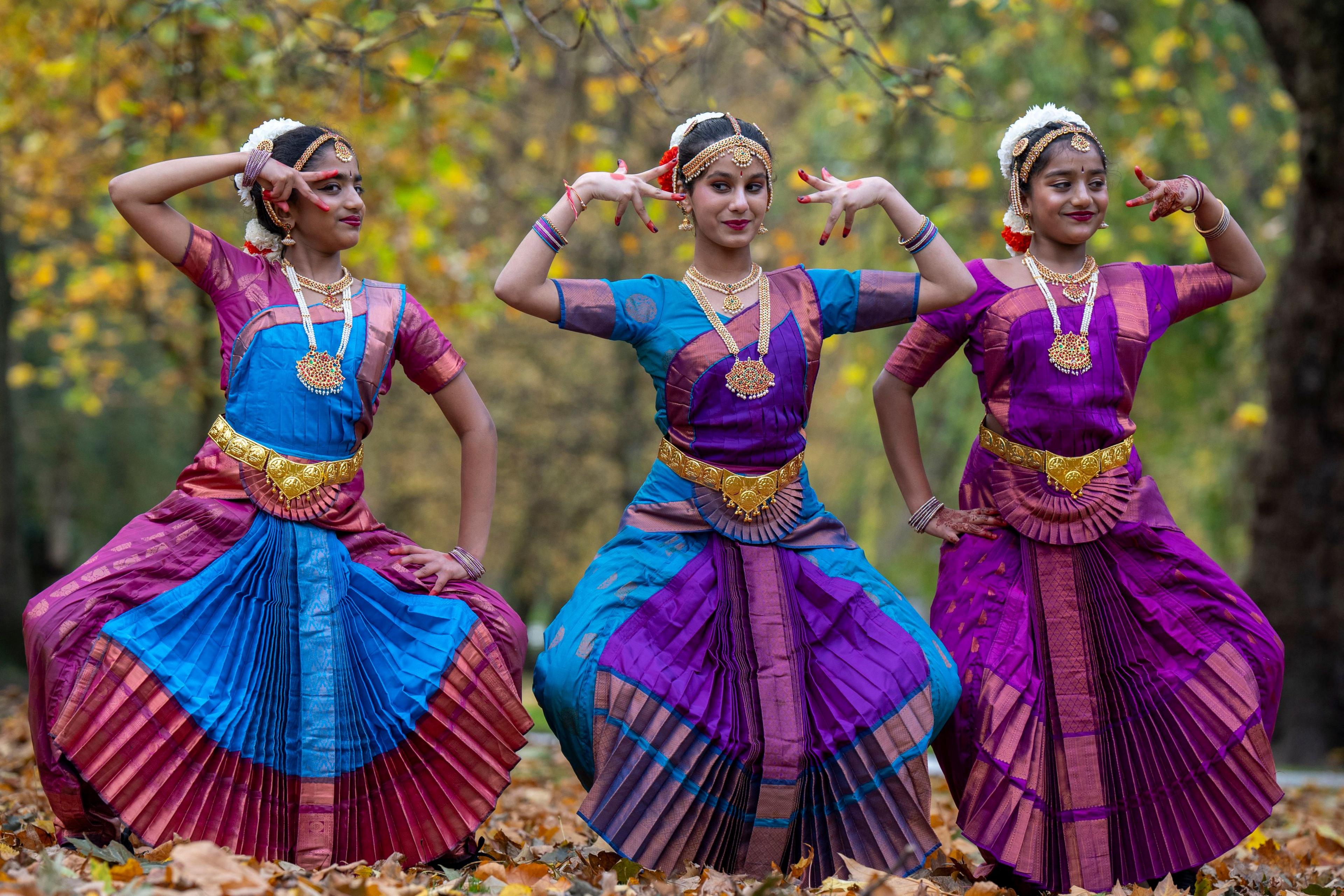 three young dancers pose wearing matching outfits and wearing flowers in their hair with elaborate jewellery.