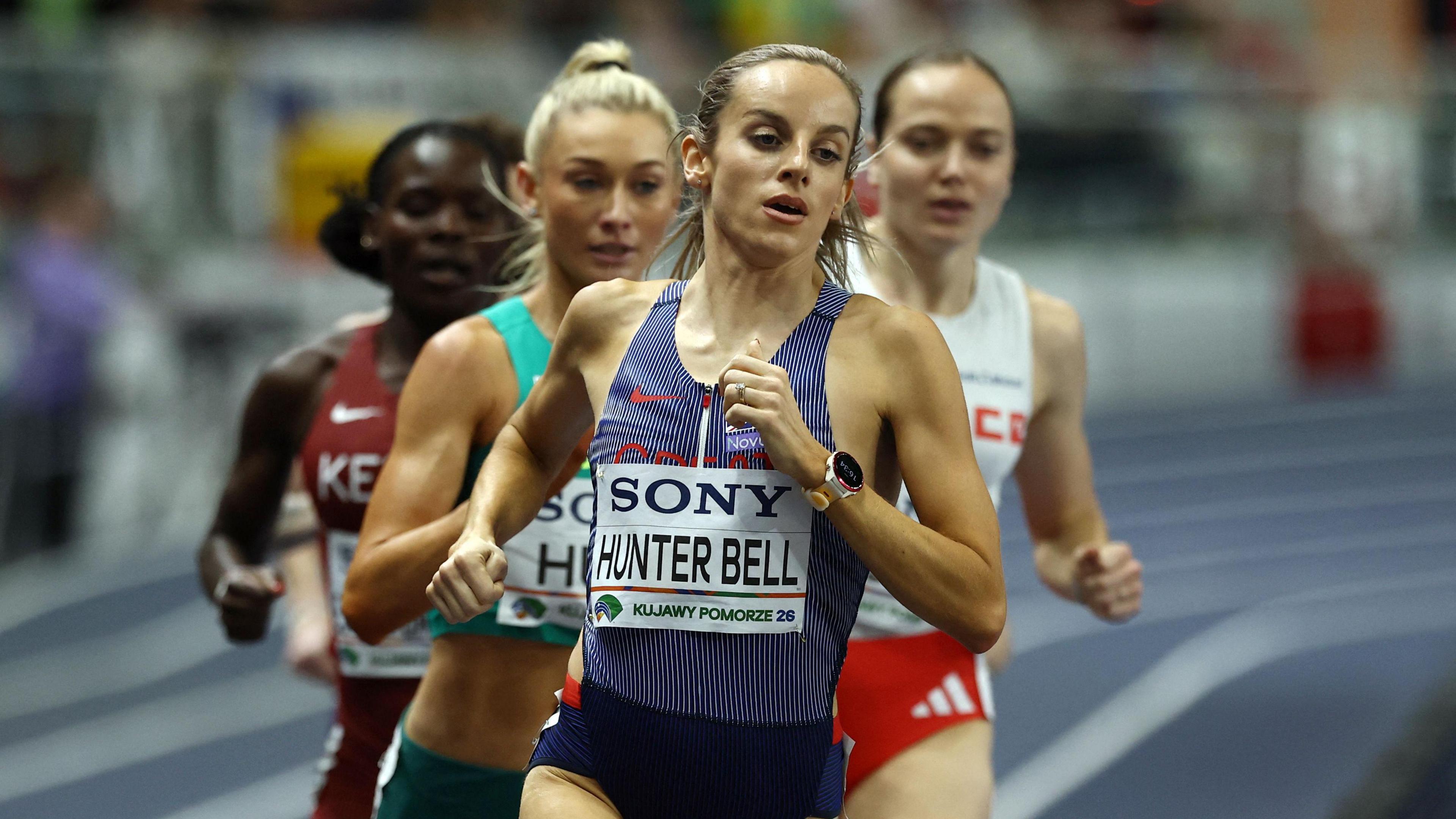 Georgia Hunter Bell competes in the 1500m. She is front of the pack with four other women running behind her. She looks focused as she concentrates on the track in front of her