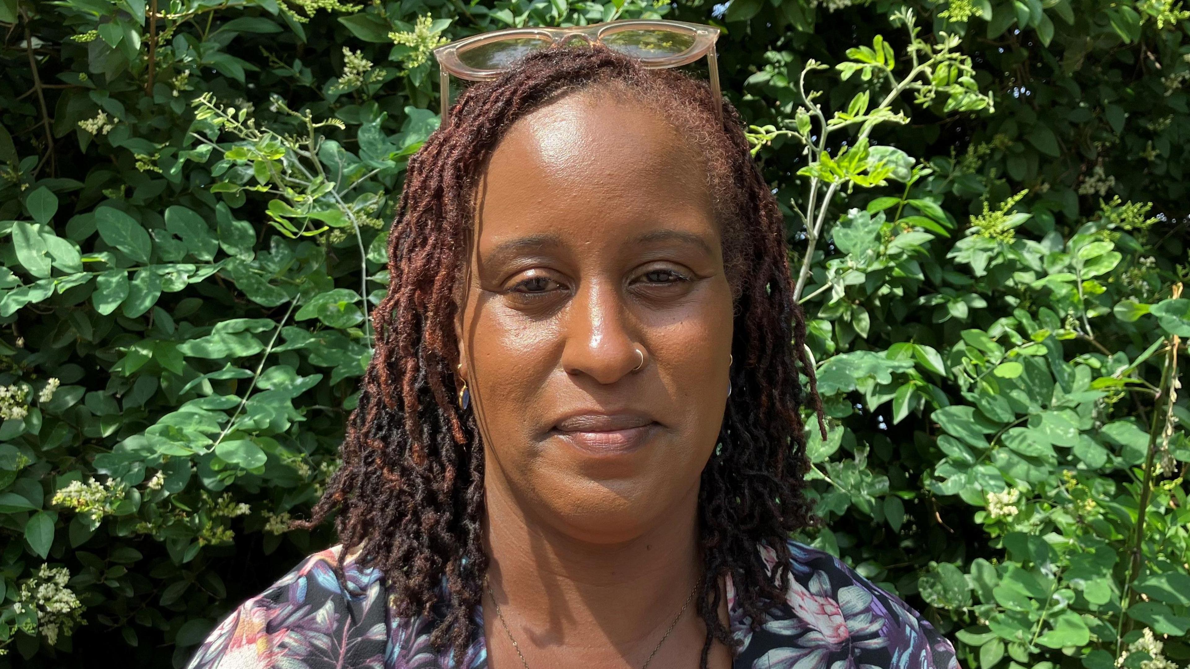 Tanya Obeng in front of green foliage. She wears glasses on her head.