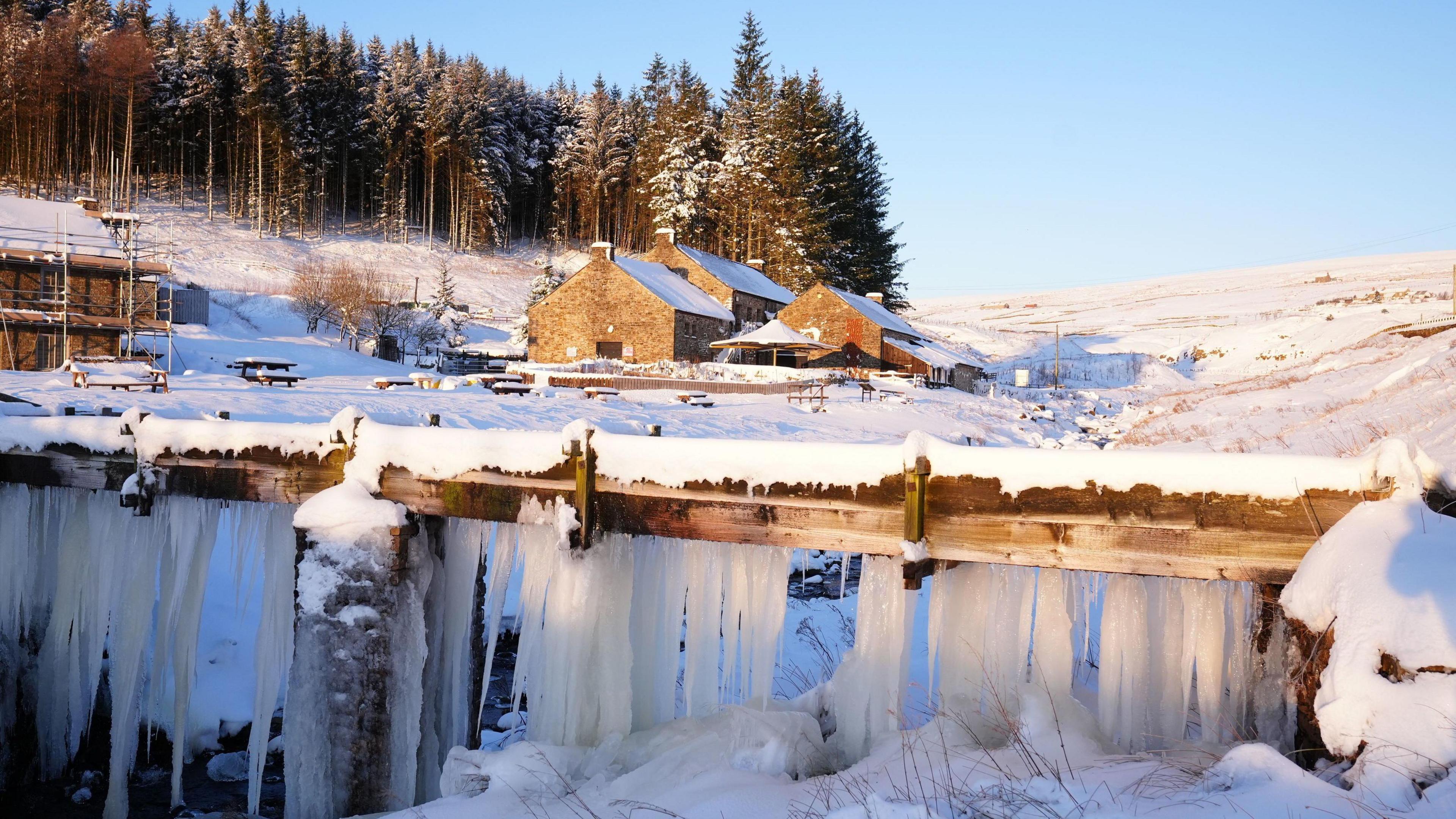 Icicles hang from a wooden bar with several buildings and hills covered in snow in the background in Durham