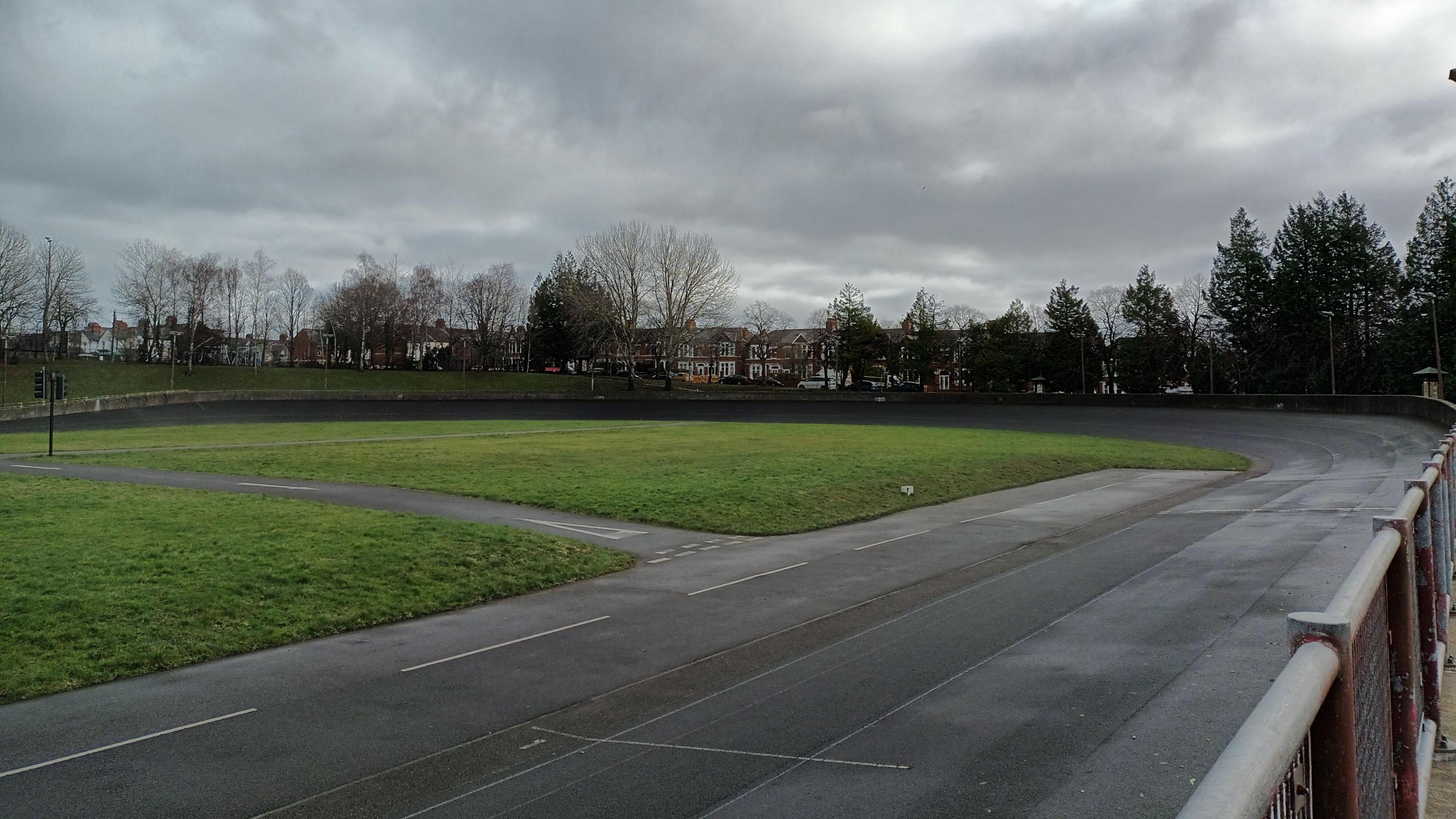 The historic velodrome. You can see the tarmac track round the edges. grassy middle sections and trees and houses in the background.