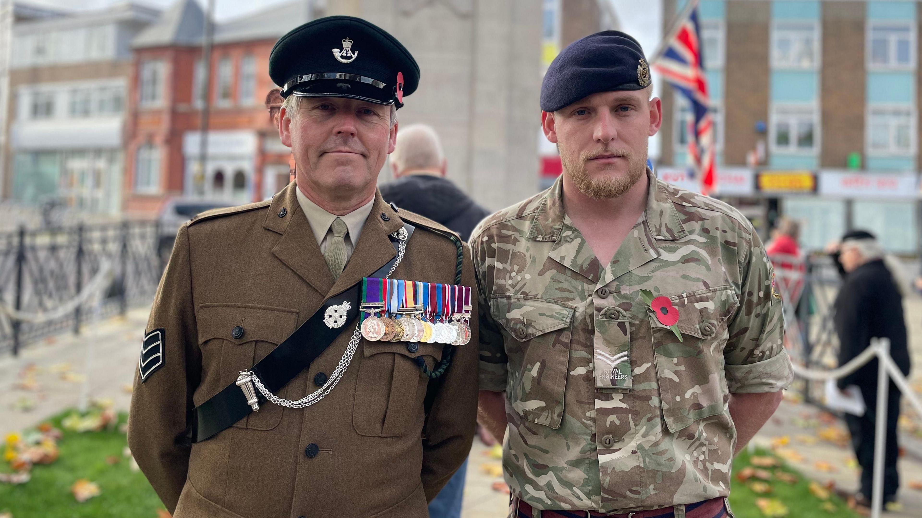 Two members of the armed forces in uniform stand in front of a cenotaph on Regent Circus in Swindon.