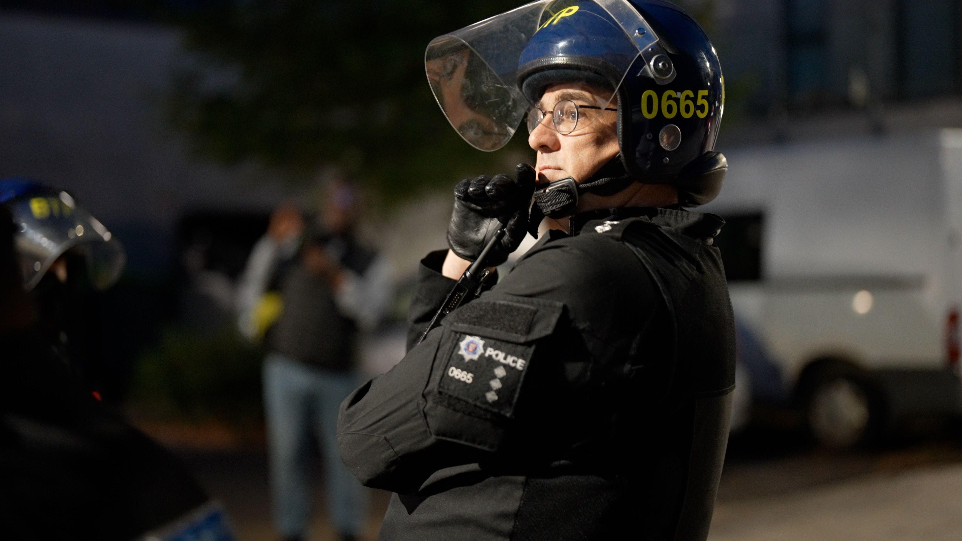 Chief Inspector Nick Brandon dressed in a protective vest and helmet looking pensively as officers line up ahead of a raid.