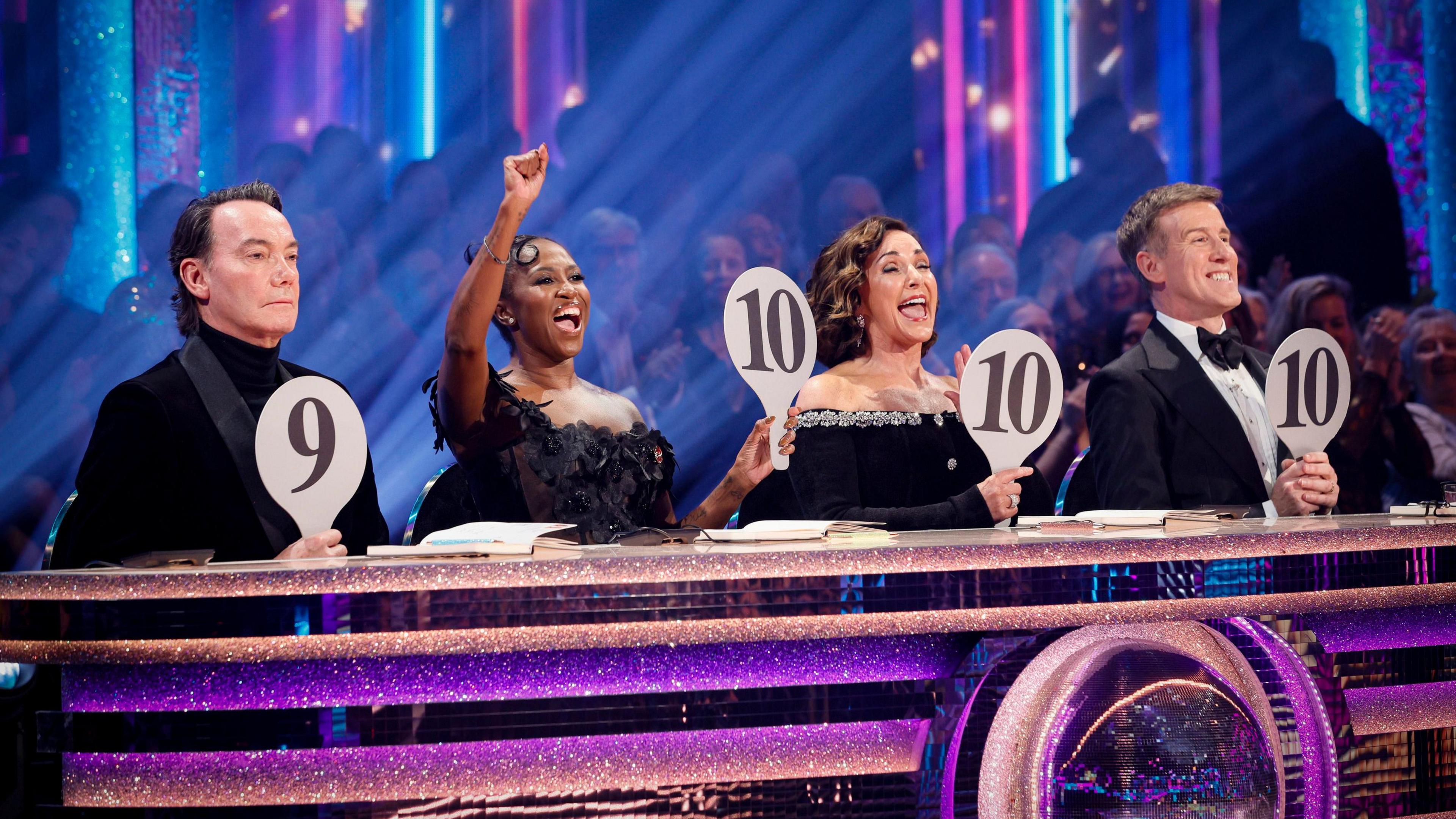 Craig, Motsi, Shirley and Anton sit at the judges desk holding up padels with numbers on. Craig is holding up a 9 with a stoney face, the other are holding up 10s and cheering