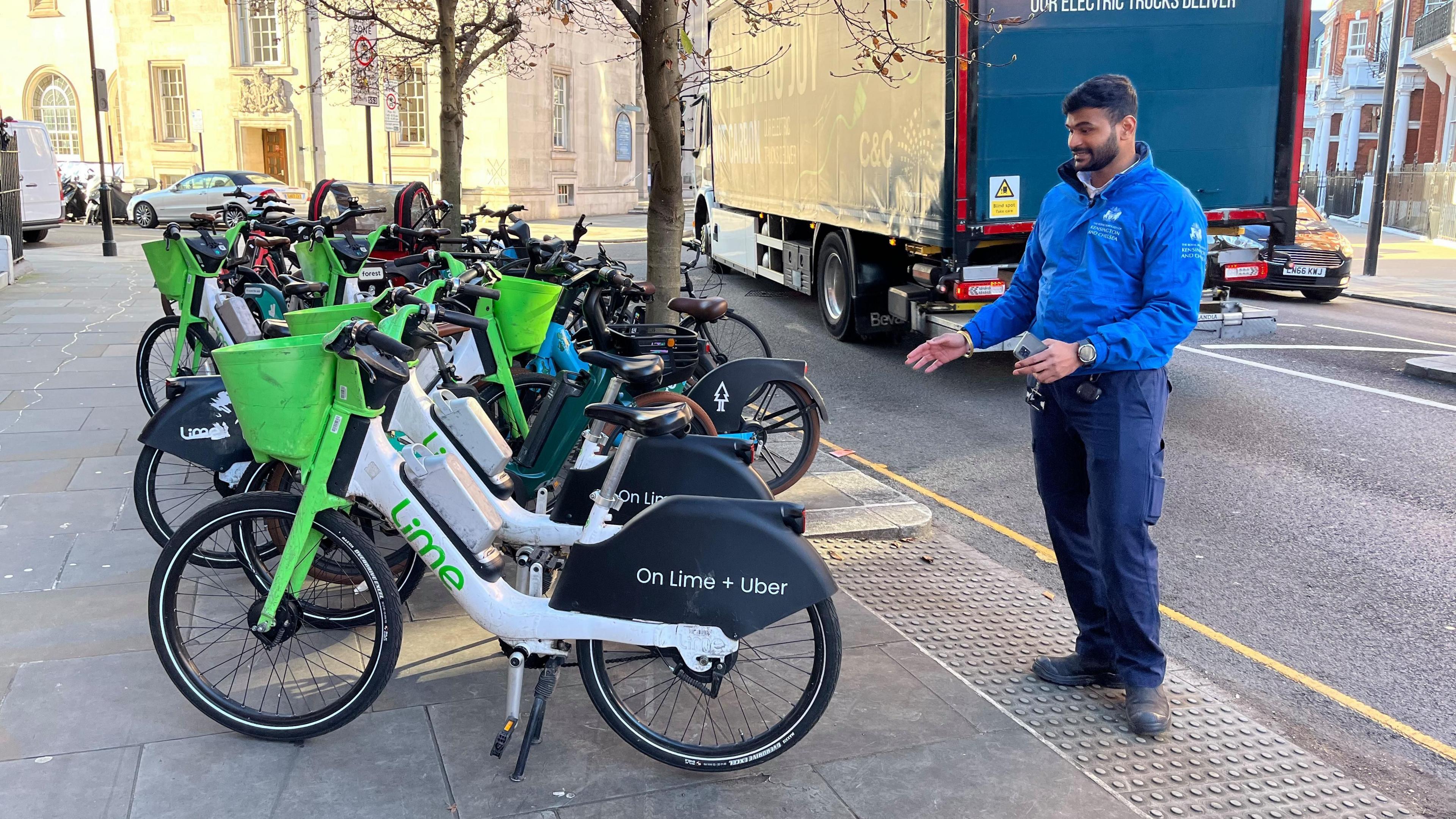 A man in a blue anorak is pointing at a Lime e-bike which is parked in front of a ramp. It is blocking the ramp.