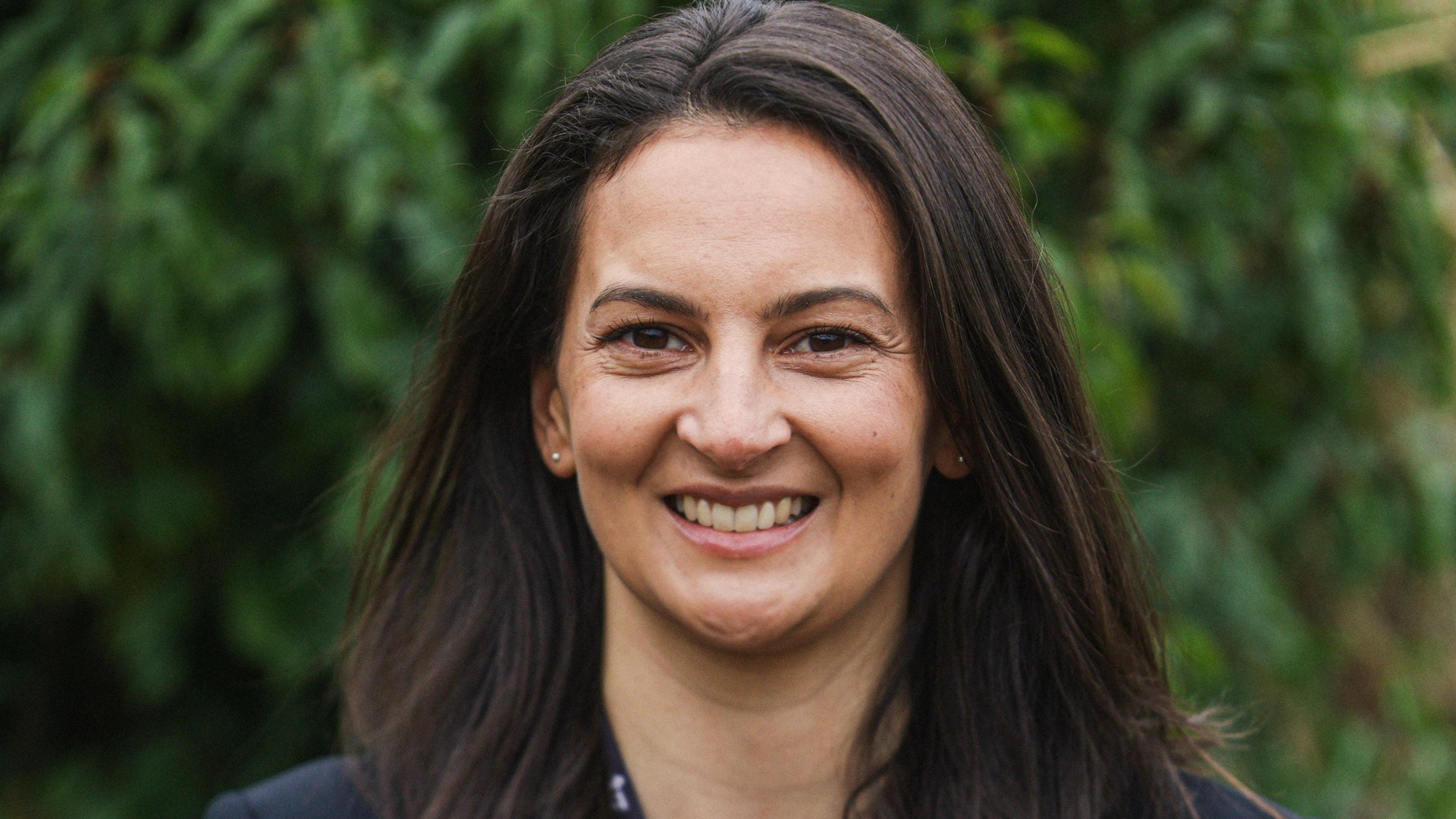 Dr Rebecca Biddle, who has long dark hair, smiling at the camera.