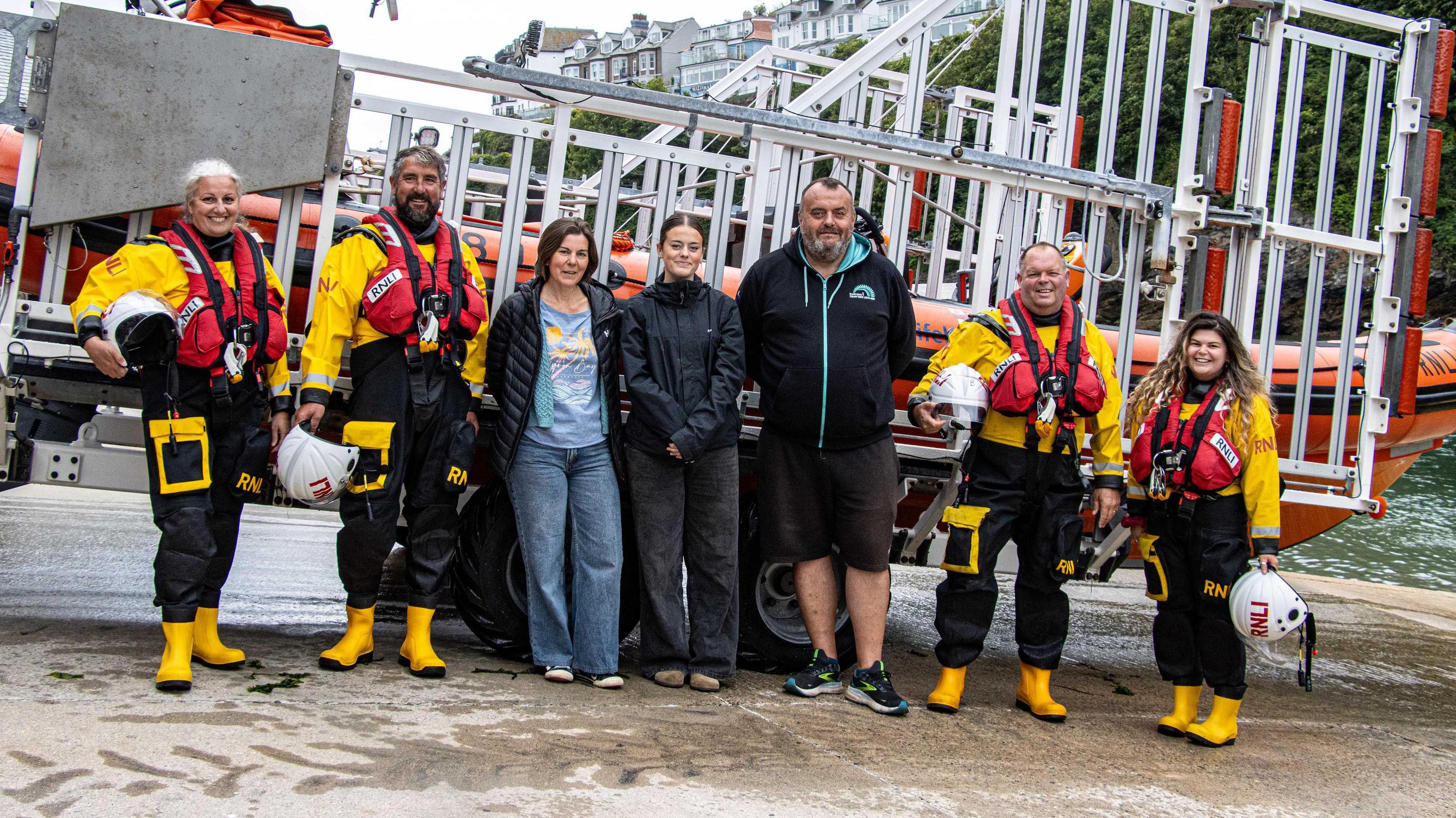 Rachel, Evie and Paul Toms with Looe RNLI volunteer crew members Victoria, David, Clive and Amber. They are stood in front of one of the crew's boats after it has returned from an incident