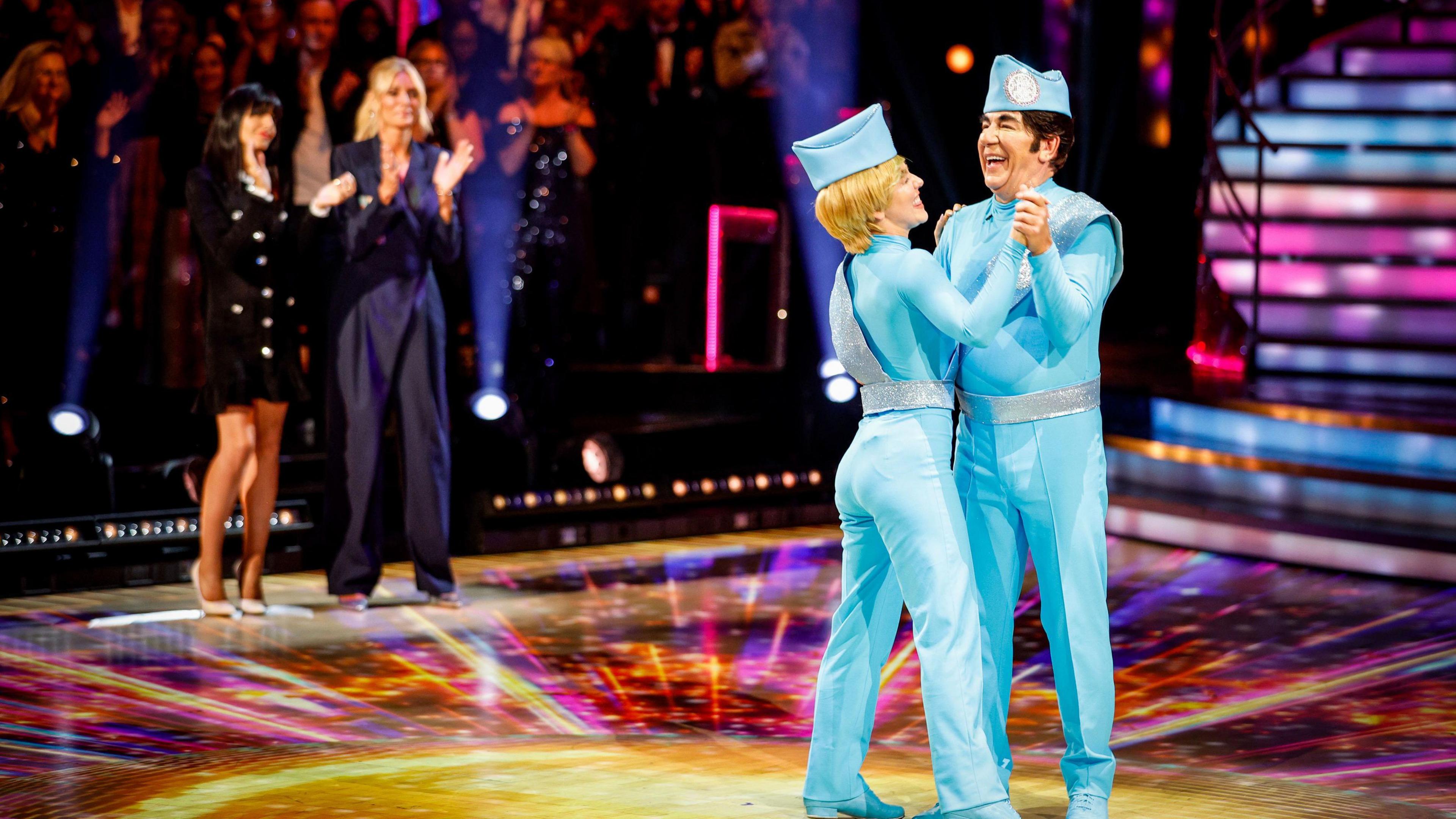 Ross King and Jowita are dressed as Thunderbirds and are dancing on stage. The audience is applauding them.